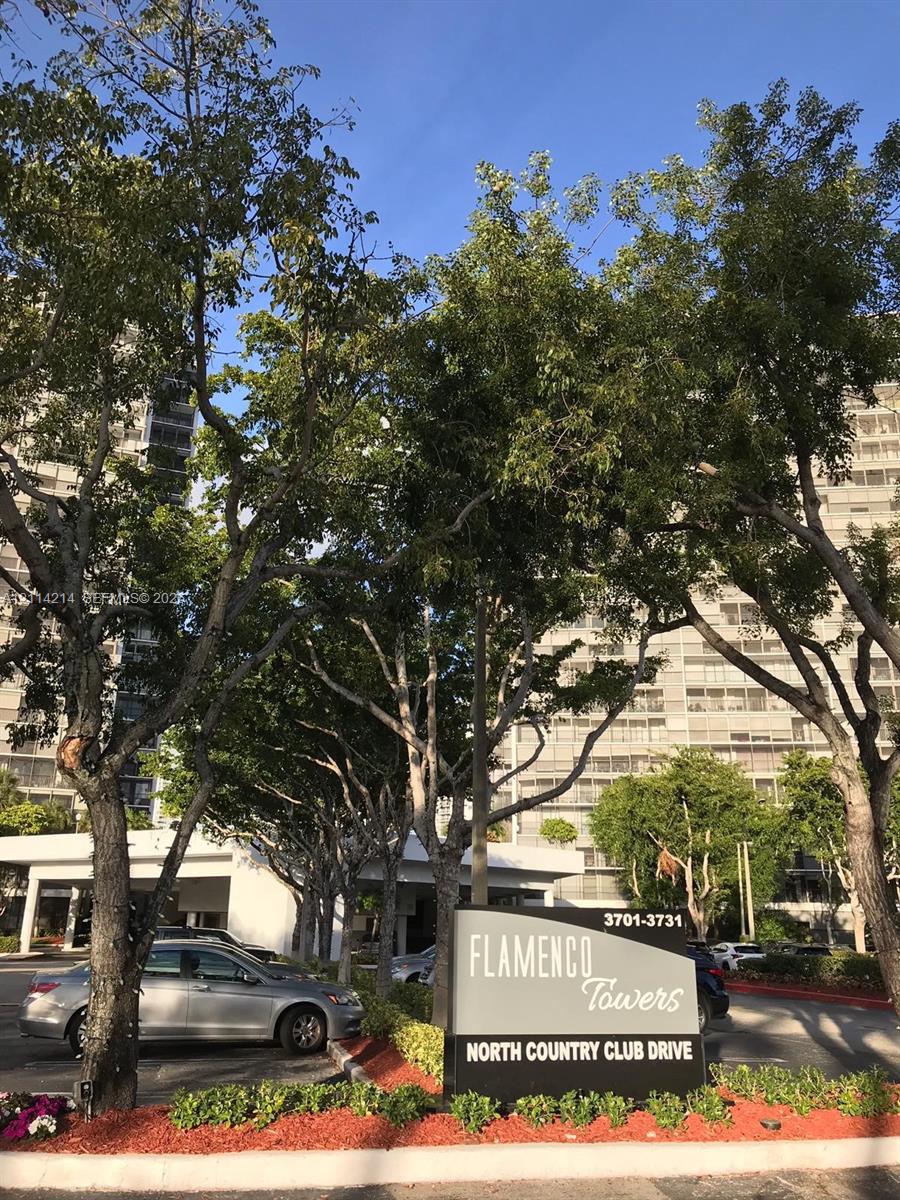 Flamenco Towers monument signage featuring high-rise building architecture, mature canopy trees, and landscaped garden beds