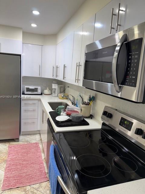 Kitchen featuring high-gloss white cabinetry, solid surface countertops, stainless steel appliances, and tiled flooring