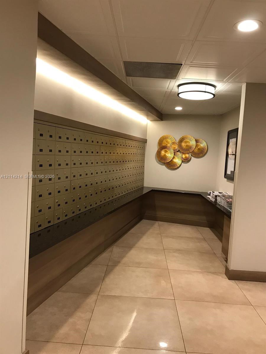 Mail center featuring integrated metallic mailboxes, recessed ceiling lighting, wall-mounted ambient lighting, neutral tile flooring, and custom cabinetry
