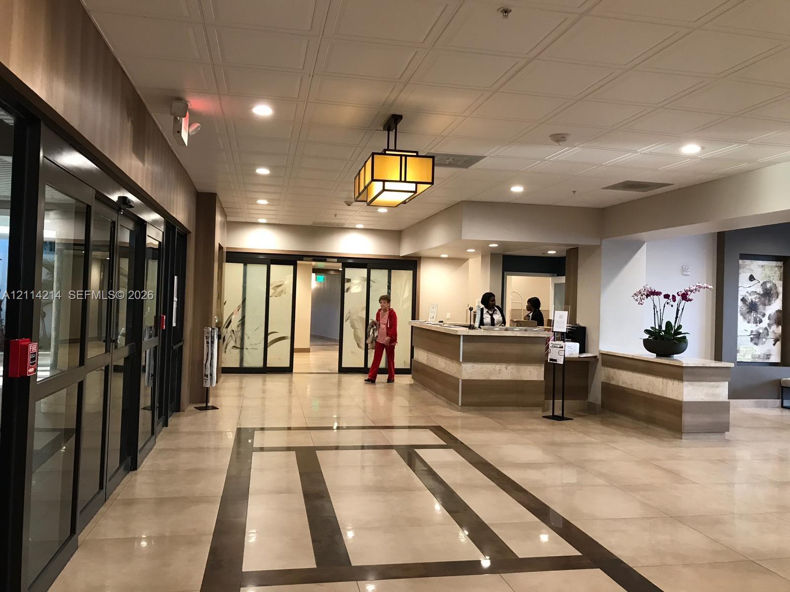 Lobby featuring tile flooring with decorative stone inlay, coffered ceiling, custom reception desk with stone detailing, glass-paneled sliding entry doors, and geometric mission-style pendant lighting