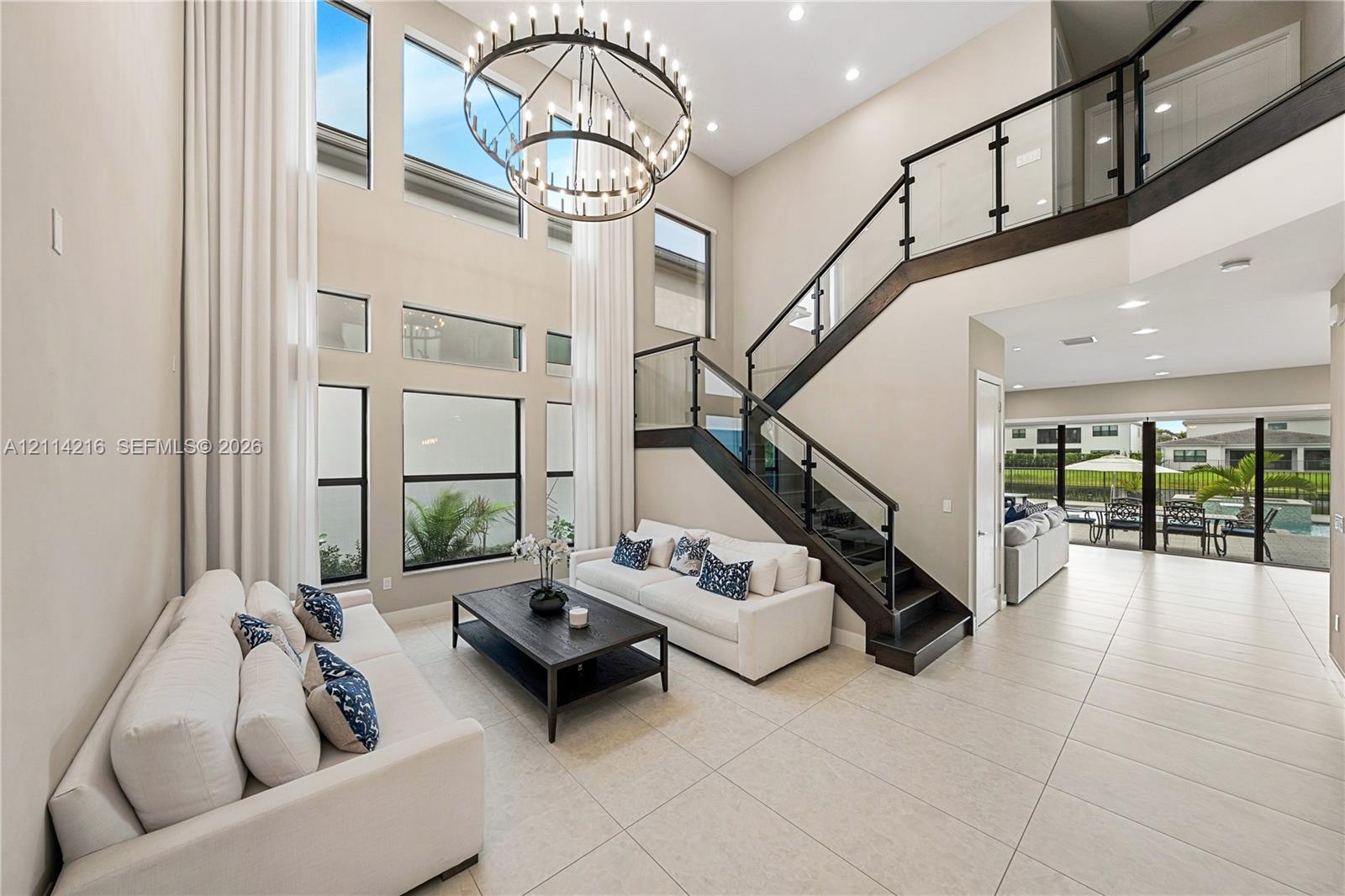 Two-story foyer featuring a floor-to-ceiling window wall, a modern multi-tier circular chandelier, and a custom staircase with glass panels and dark wood-finish railings