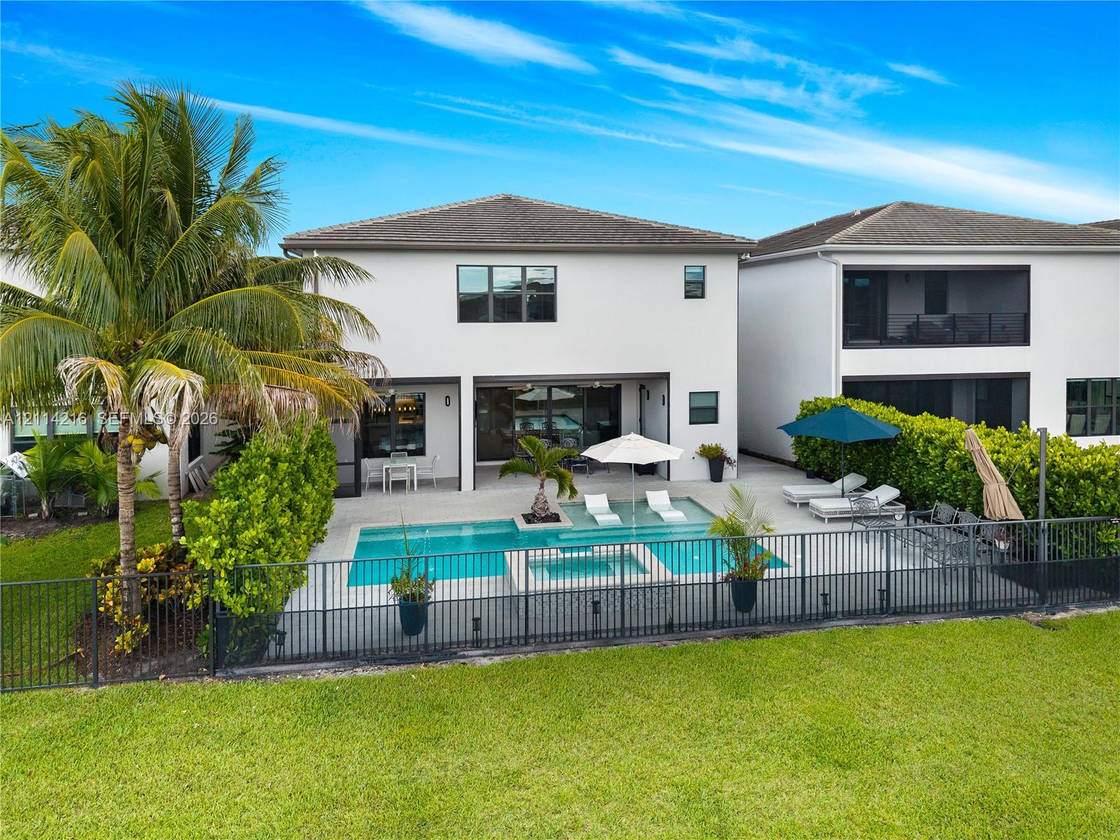 Rear exterior featuring a swimming pool with integrated spa, a paver patio, metal perimeter fencing, and established privacy hedges
