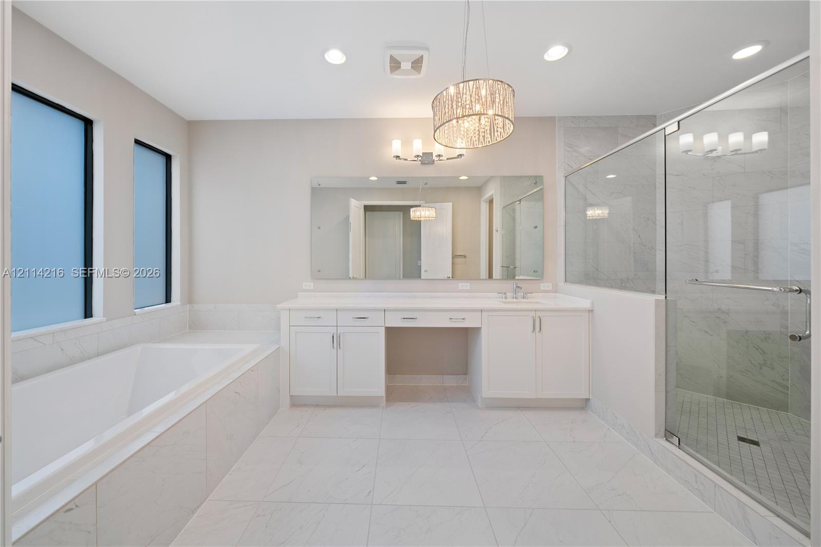 Bathroom featuring a walk-in shower with glass enclosure, soaking tub with tile surround, white cabinetry, integrated vanity, and decorative pendant lighting
