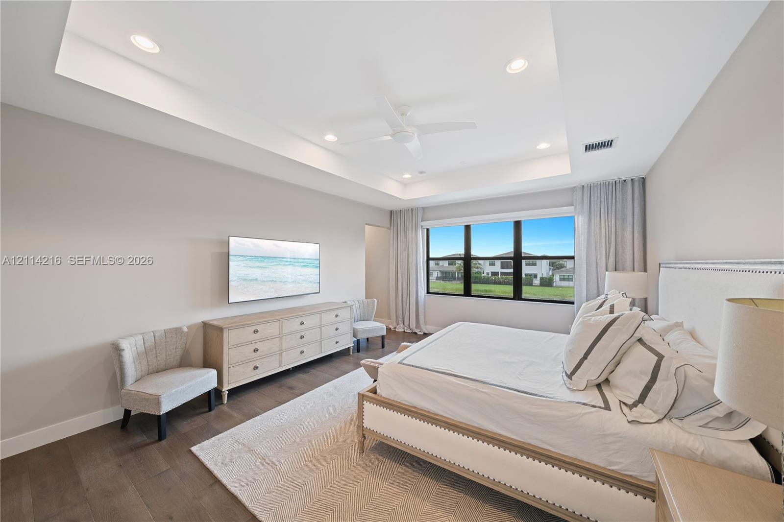 Tray ceiling with integrated recessed lighting, ceiling fan, wood-finish flooring, and multi-pane window