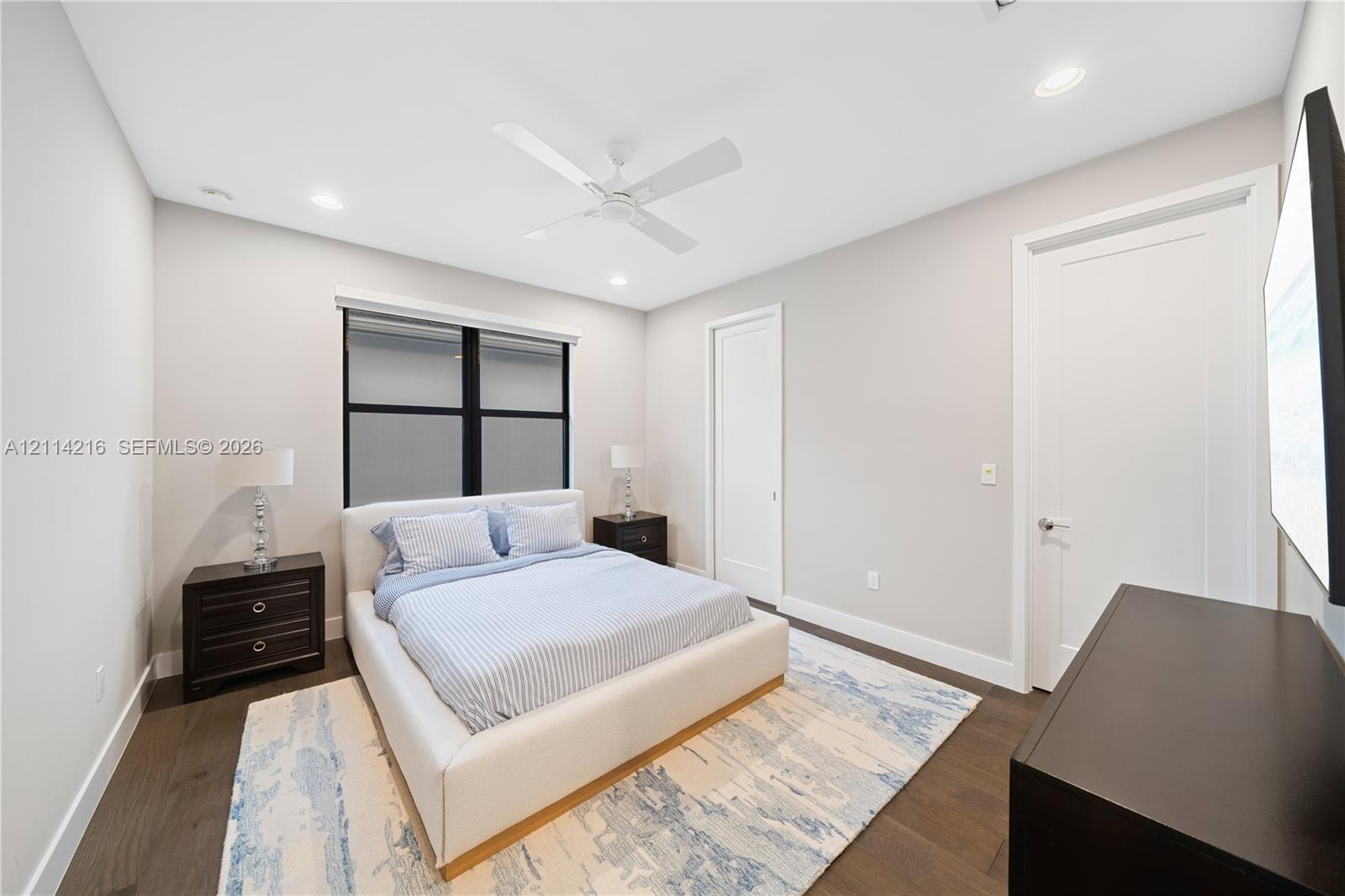 Neutral-toned interior room featuring wood-finish flooring, a white ceiling fan, recessed lighting, and a window with black trim