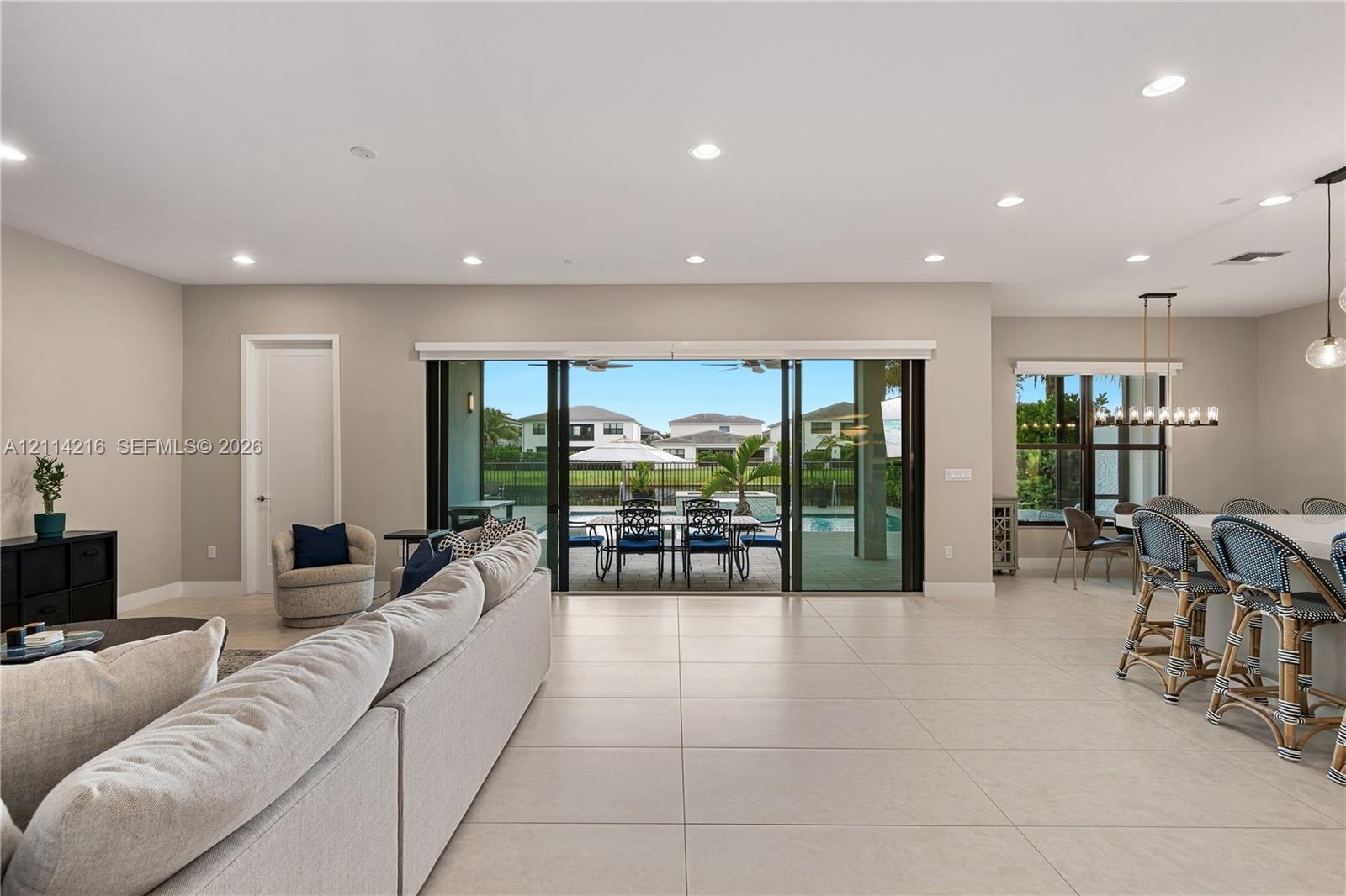 Open-concept interior featuring large-format tile flooring, recessed ceiling lighting, and expansive multi-panel sliding glass doors opening to a covered patio