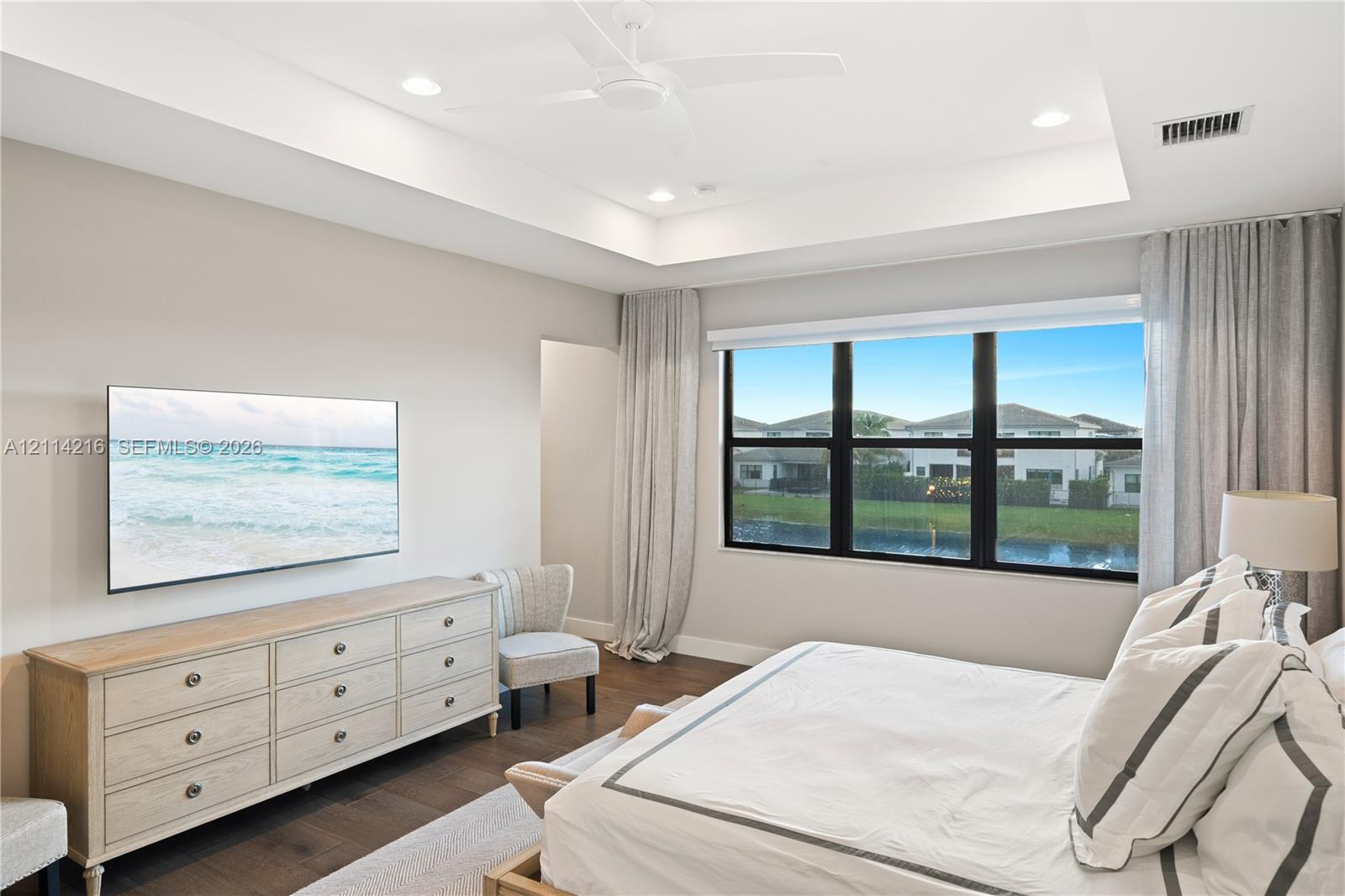 Tray ceiling with recessed lighting and a central ceiling fan, large windows with dark frames, and wood-finish flooring