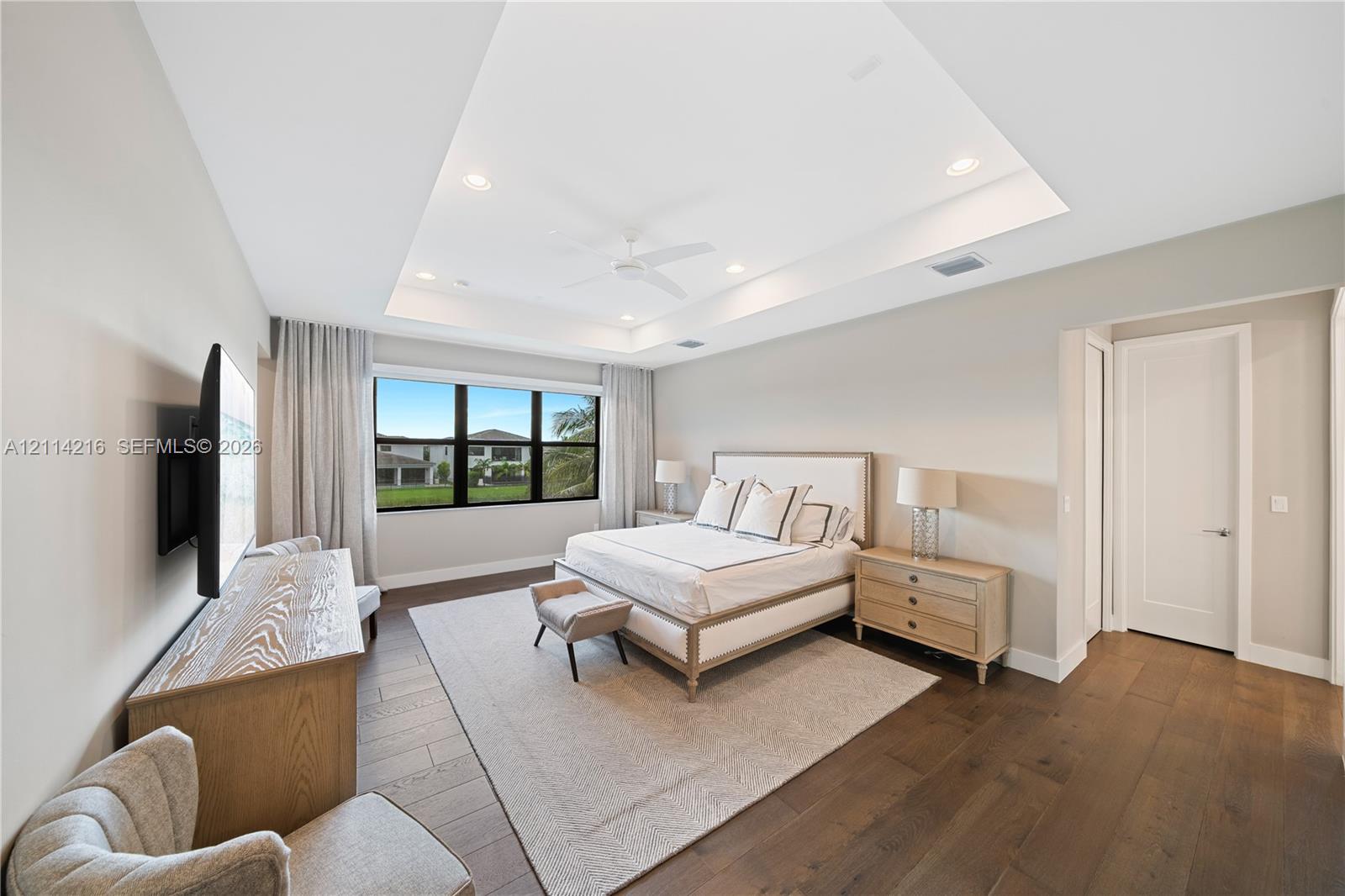 Tray ceiling with recessed lighting, wide-plank wood-finish flooring, and black-framed windows