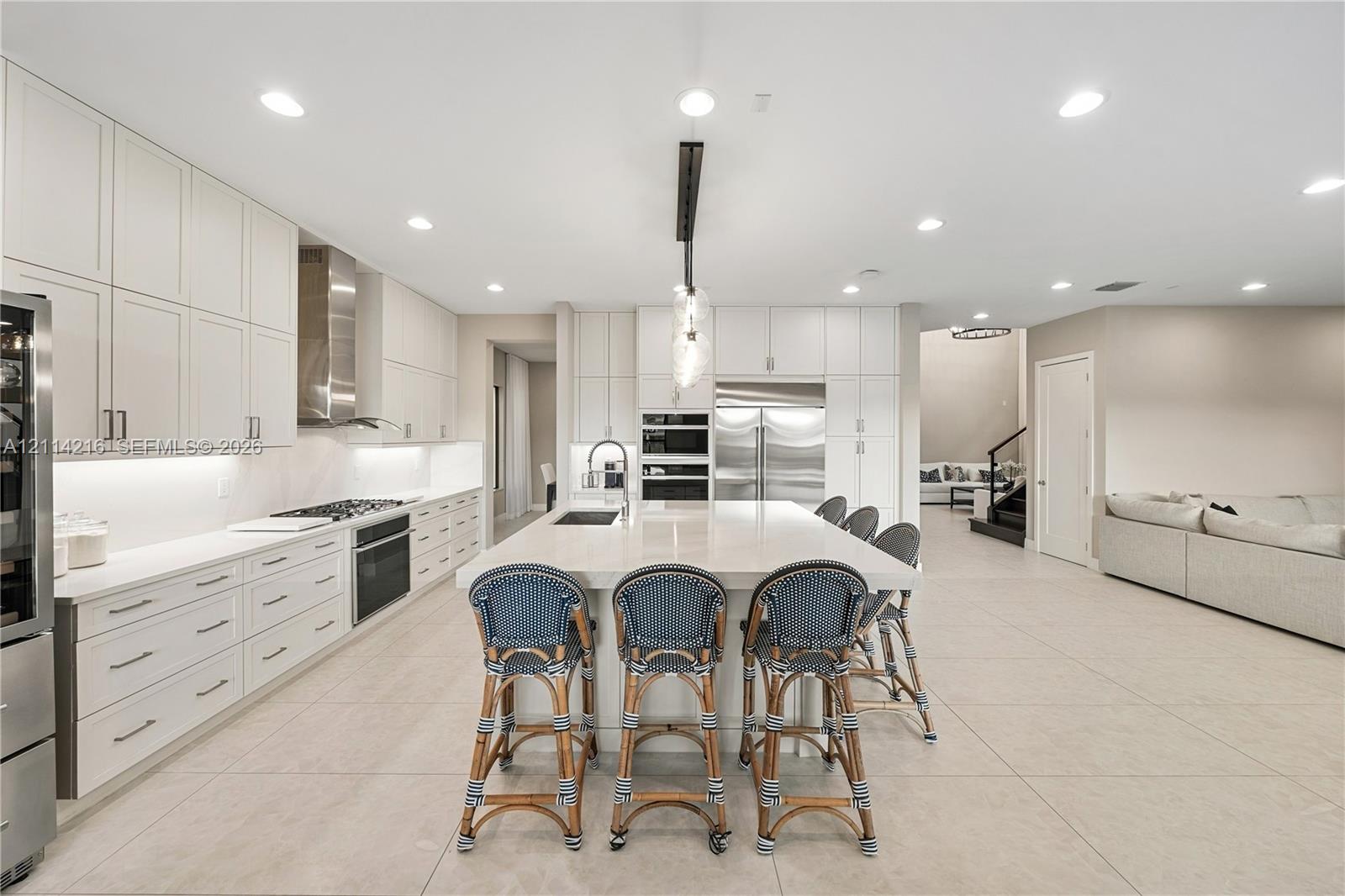 Contemporary kitchen featuring ceiling-height flat-panel cabinetry, a central island with a stone-finish countertop, stainless steel built-in appliances, recessed lighting, and large-format tile flooring