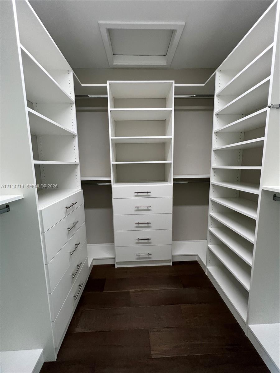 Custom walk-in closet featuring extensive white built-in shelving, multiple integrated storage drawers with brushed nickel hardware, and dark wood-finish flooring