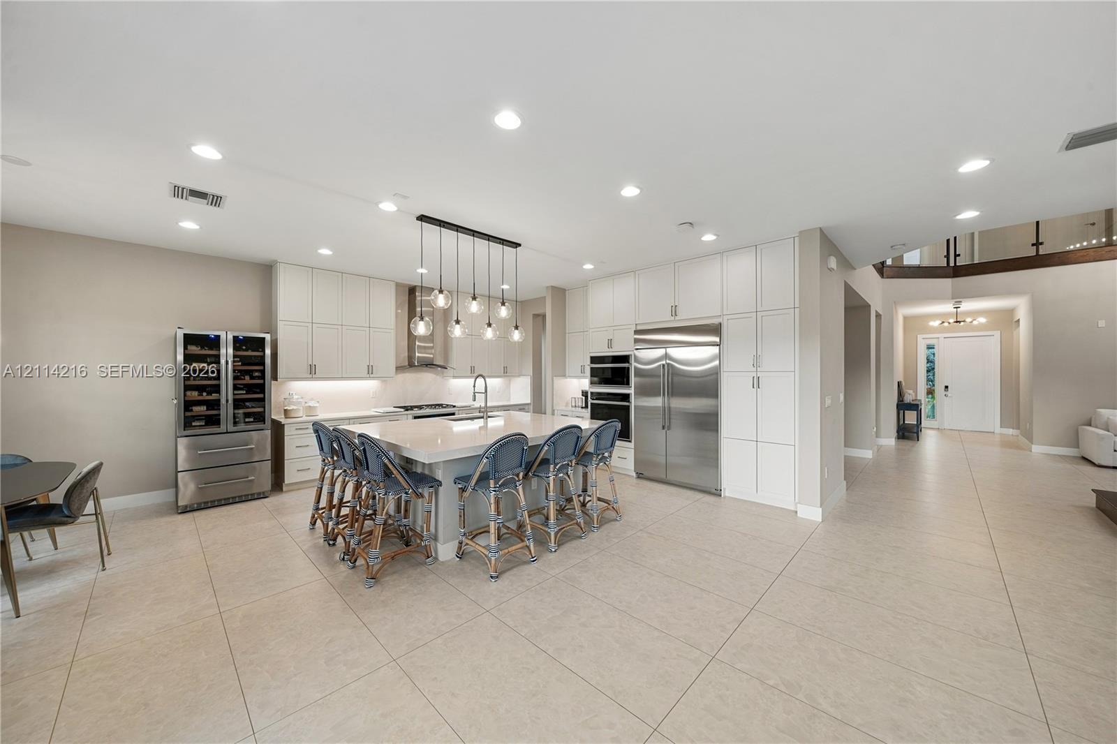 Kitchen featuring floor-to-ceiling white cabinetry, a large central island with quartz countertops, integrated stainless steel appliances, built-in wine refrigeration, and recessed ceiling lighting
