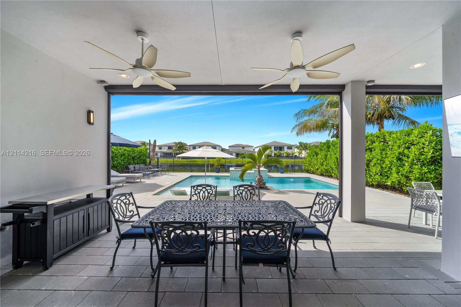 Covered patio featuring large-format tile flooring, dual ceiling fans, and recessed lighting, overlooking a private swimming pool with a stone water feature