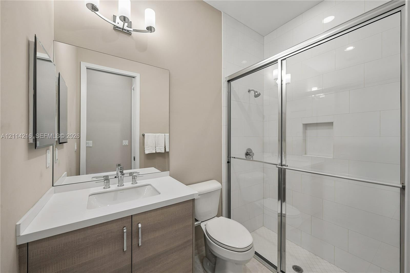 Bathroom featuring a wood-finish vanity with a stone countertop, an integrated rectangular sink, a glass-enclosed shower with subway tile surround, and an expansive wall-mounted mirror