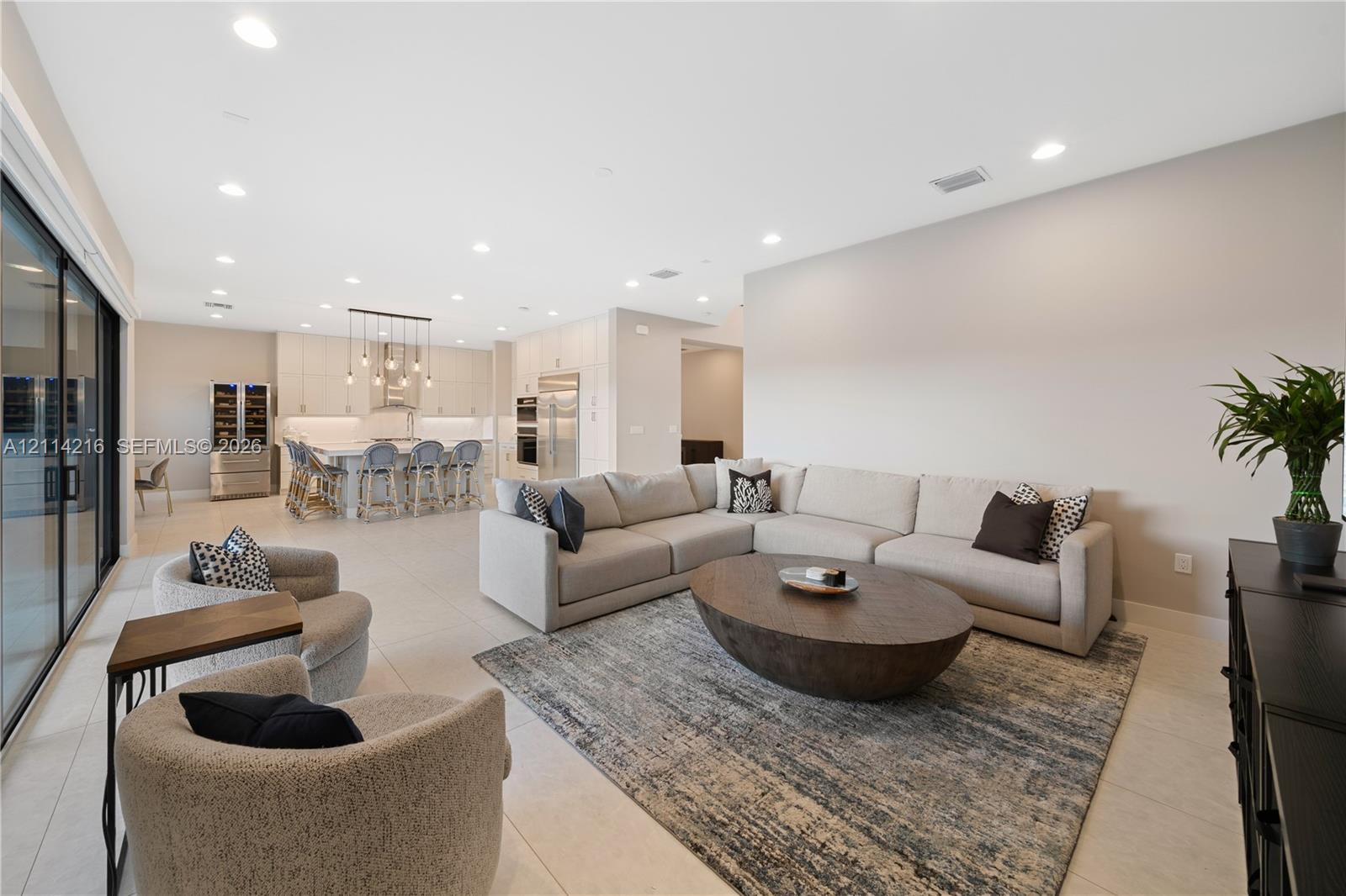 Open-concept interior featuring large-format tile flooring, recessed ceiling lighting, sliding glass doors, and a kitchen equipped with a center island and built-in stainless steel appliances