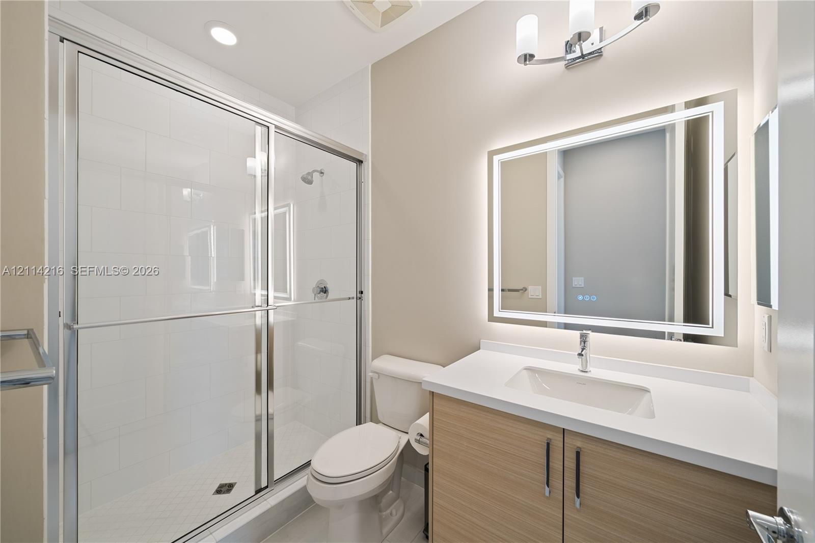 Bathroom featuring a walk-in shower with a glass enclosure, wood-finish vanity with a stone countertop, integrated undermount sink, and a modern LED-backlit mirror
