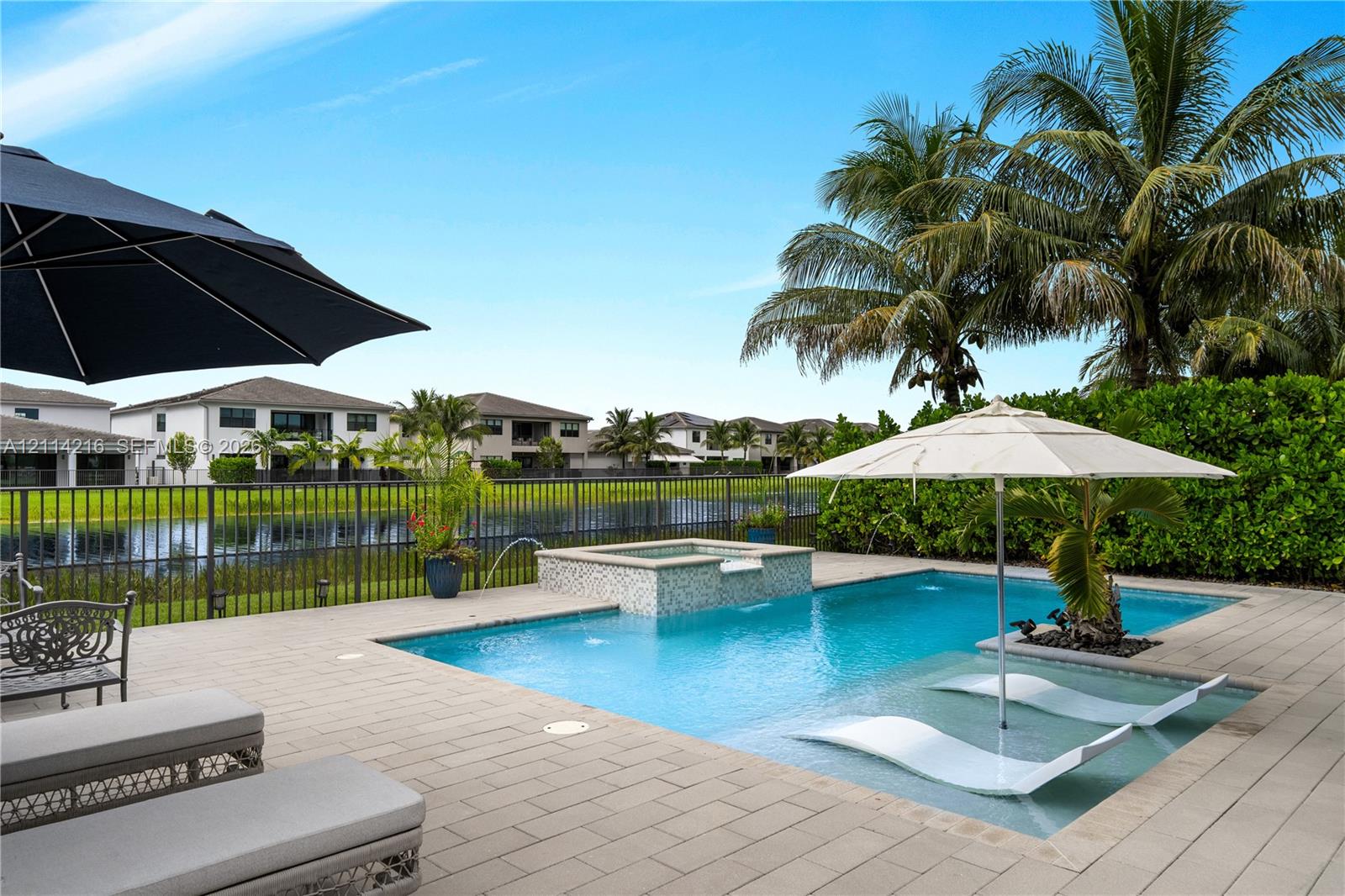 In-ground swimming pool featuring a built-in spillover spa, tanning ledge, stone-finish paver deck, and metal perimeter fencing