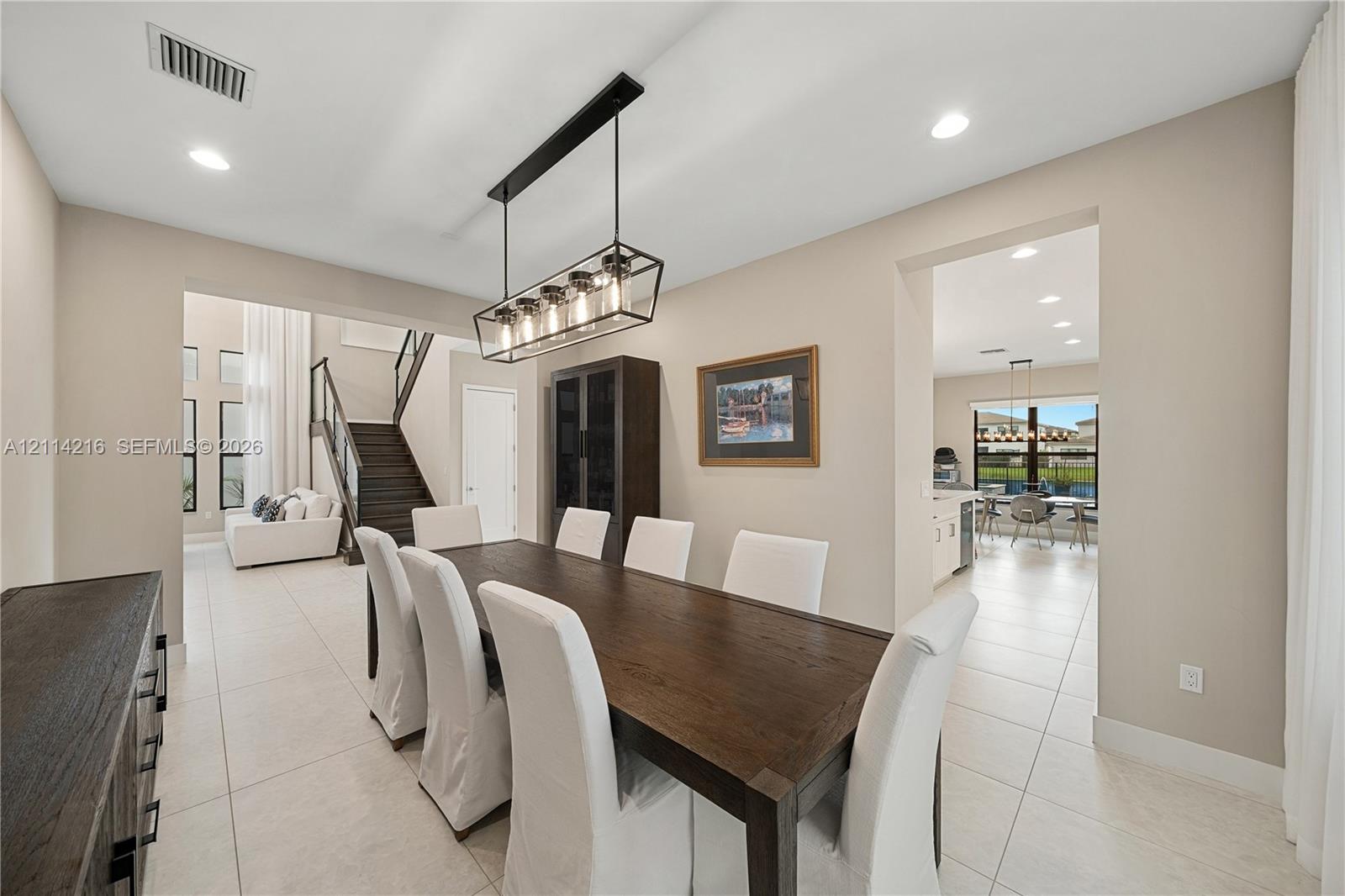 Dining area featuring oversized tile flooring, recessed lighting, and a multi-light linear pendant fixture, including a built-in floor-to-ceiling cabinet with glass-front detailing