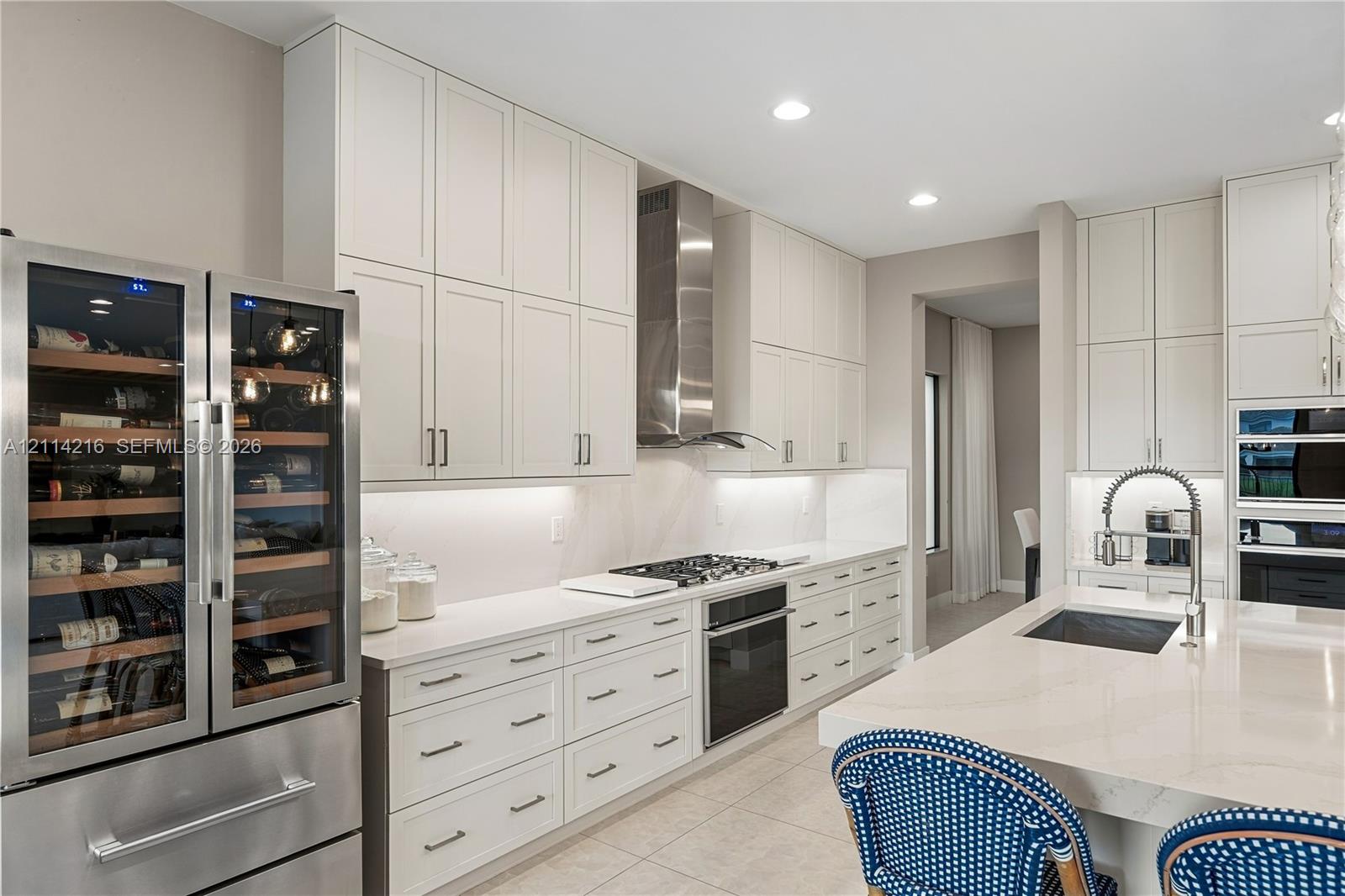 Kitchen featuring white ceiling-height cabinetry, quartz countertops, stainless steel appliance suite including a built-in wine refrigerator, and a center island with a stainless steel pull-down faucet