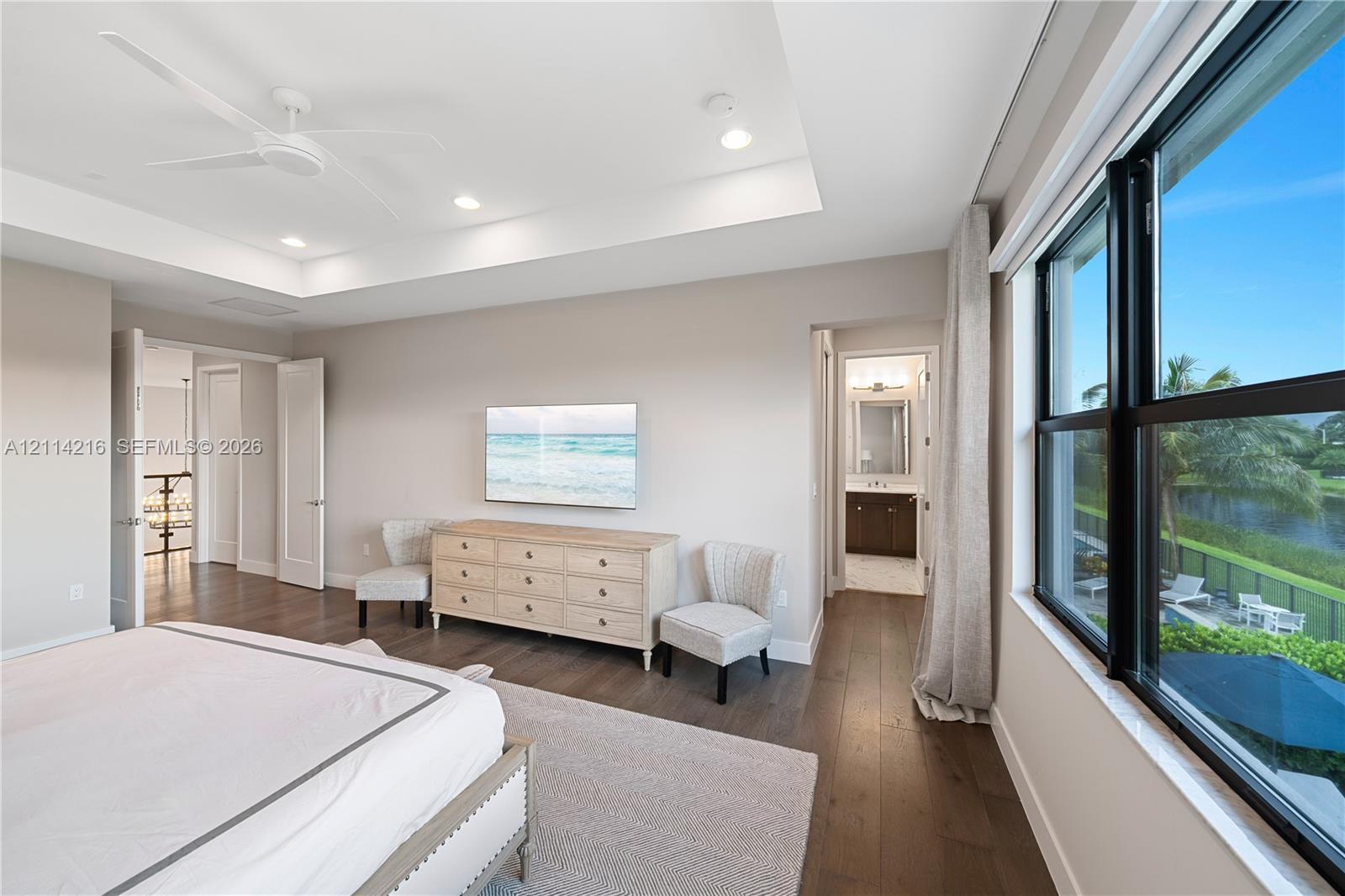 Tray ceiling, wood-finish flooring, ceiling fan, and large windows with exterior water scenery