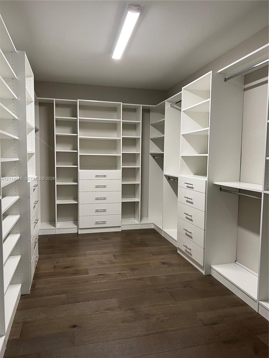 Walk-in closet featuring extensive built-in white cabinetry, integrated drawer banks, adjustable shelving, chrome hardware, and wood-finish flooring