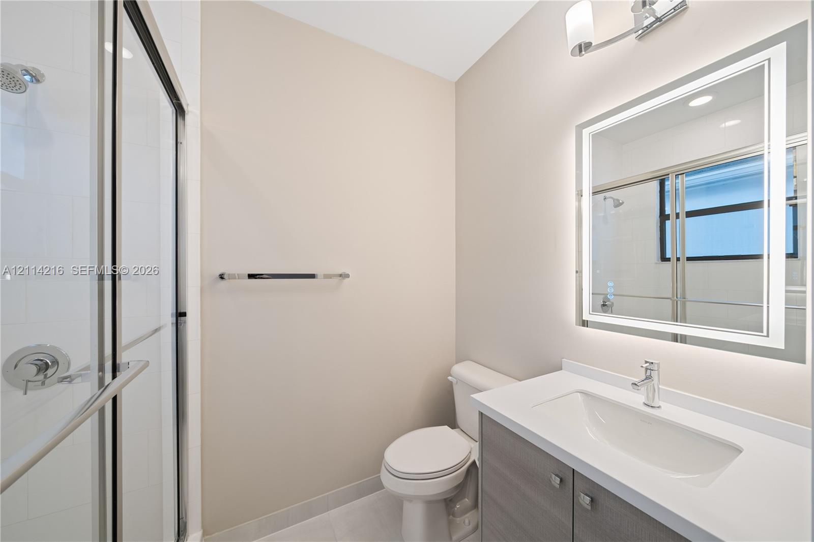 Bathroom featuring a glass-enclosed shower, integrated vanity with a rectangular sink, wall-mounted illuminated mirror, and polished chrome hardware