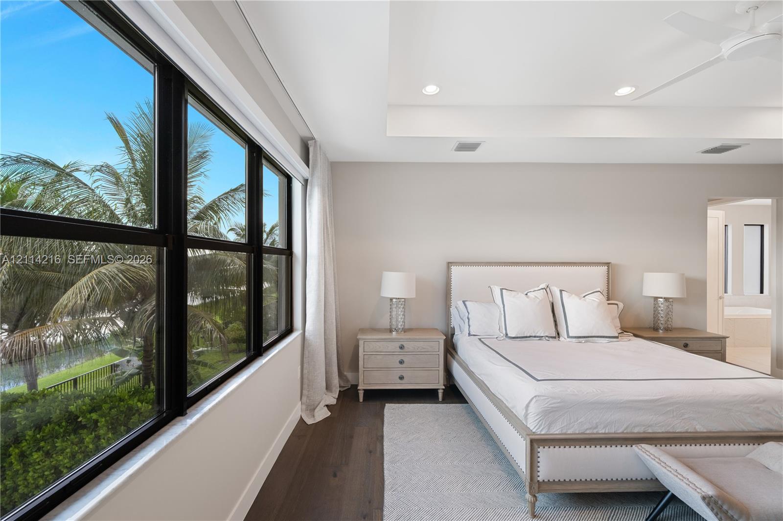 Large windows with black frames, tray ceiling with recessed lighting, and dark wood-finish flooring
