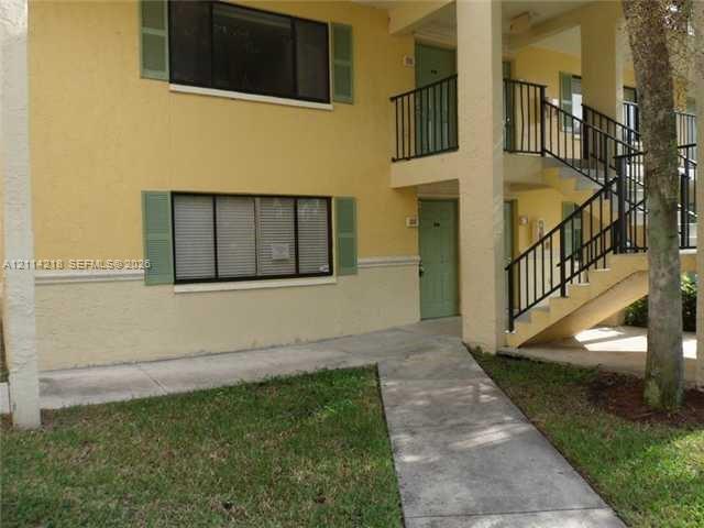 Two-story exterior featuring a painted stucco facade, operable shutters, tiered concrete walkways, and black metal railings