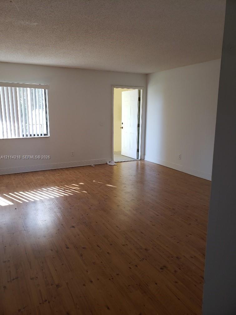 Wood-finish flooring, neutral walls, and window with vertical blinds