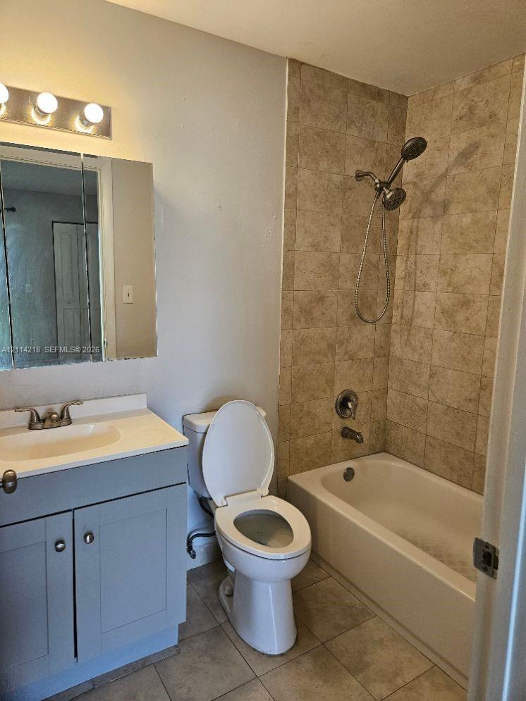 Bathroom featuring a vanity with an integrated sink, rectangular medicine cabinet, wall-mounted light fixture, and shower-tub combination with stone-finish tile surround and handheld shower head