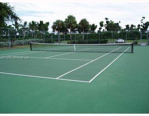 Private tennis court featuring a green surface, court markings, perimeter chain-link fencing, and mature palm trees