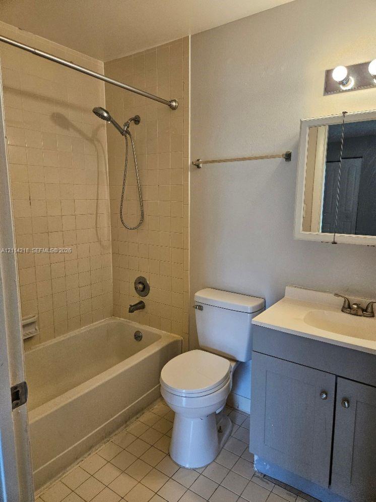Bathroom featuring a built-in vanity with a stone-top sink, ceramic tile flooring, a porcelain tub, and a shower-head fixture with integrated controls