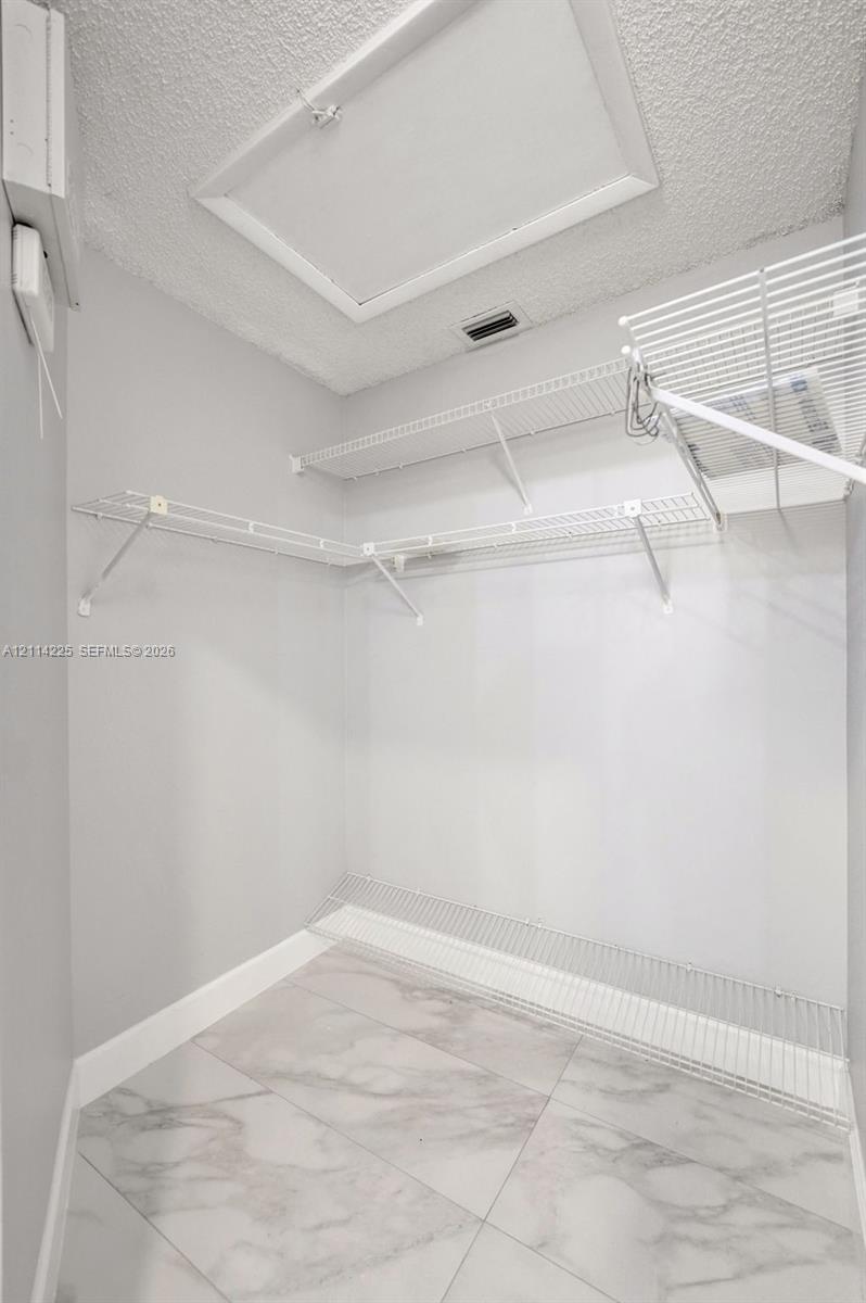 Storage area featuring large-format tile flooring, multi-level white wire shelving, and attic access panel