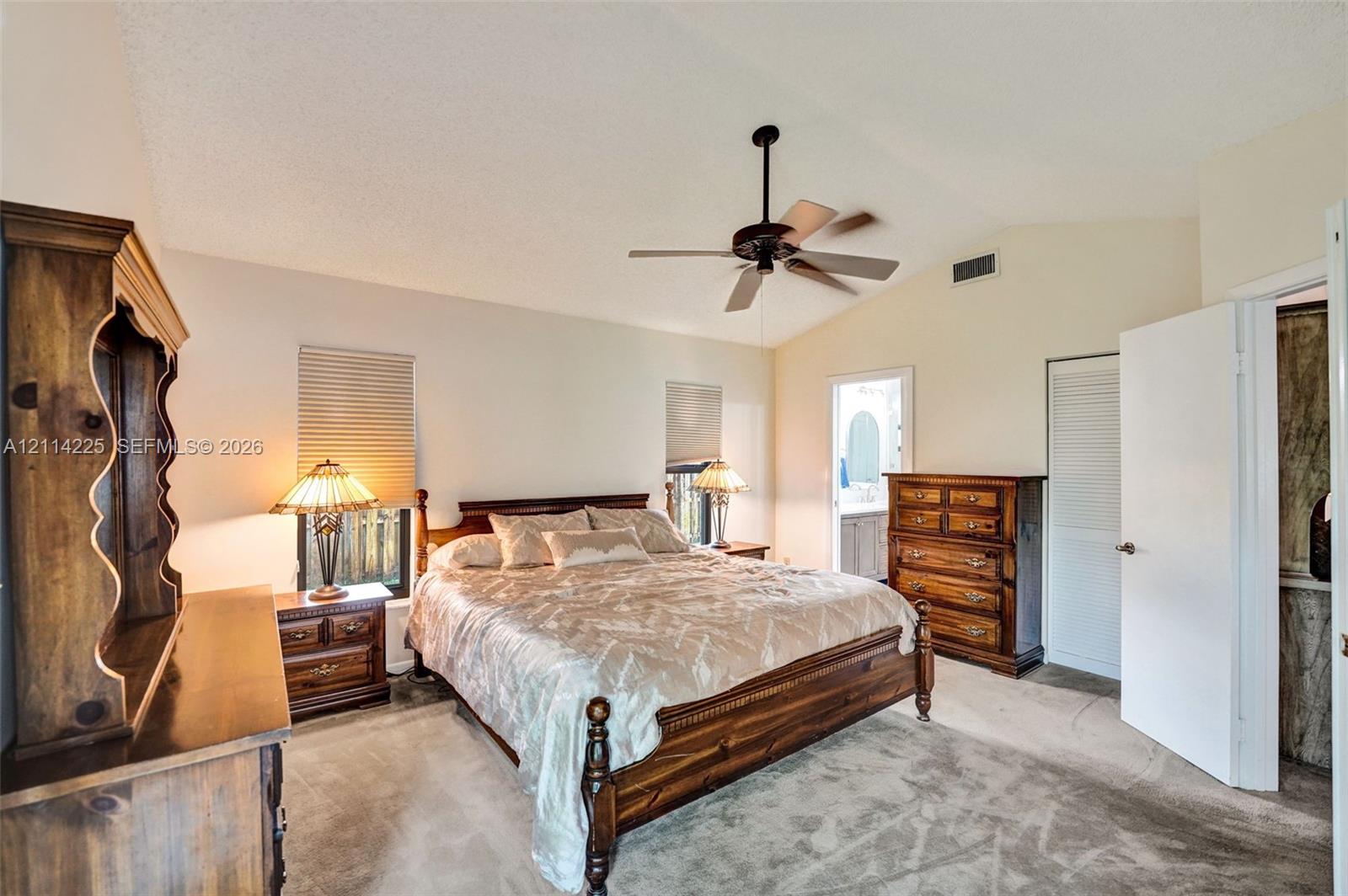 Vaulted ceiling with a centrally mounted ceiling fan, neutral wall-to-wall carpeting, and louvered closet doors