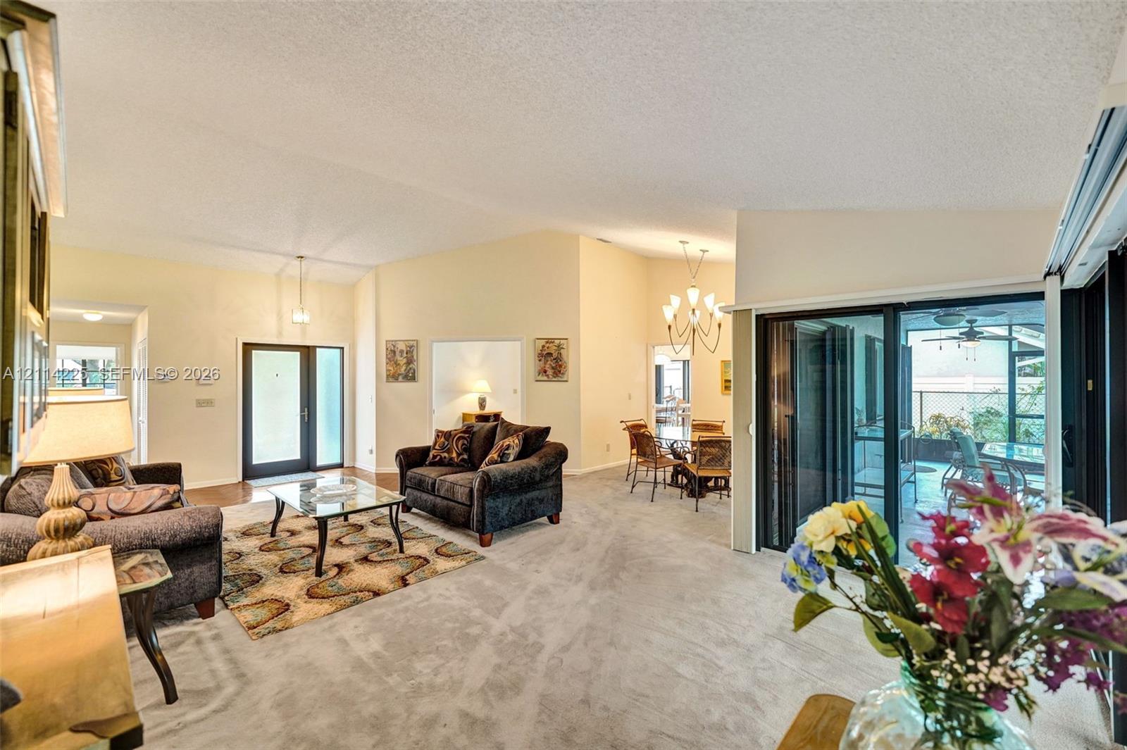 Vaulted ceilings, sliding glass doors, multi-light chandelier, front entryway with side-light panels, and neutral carpeting