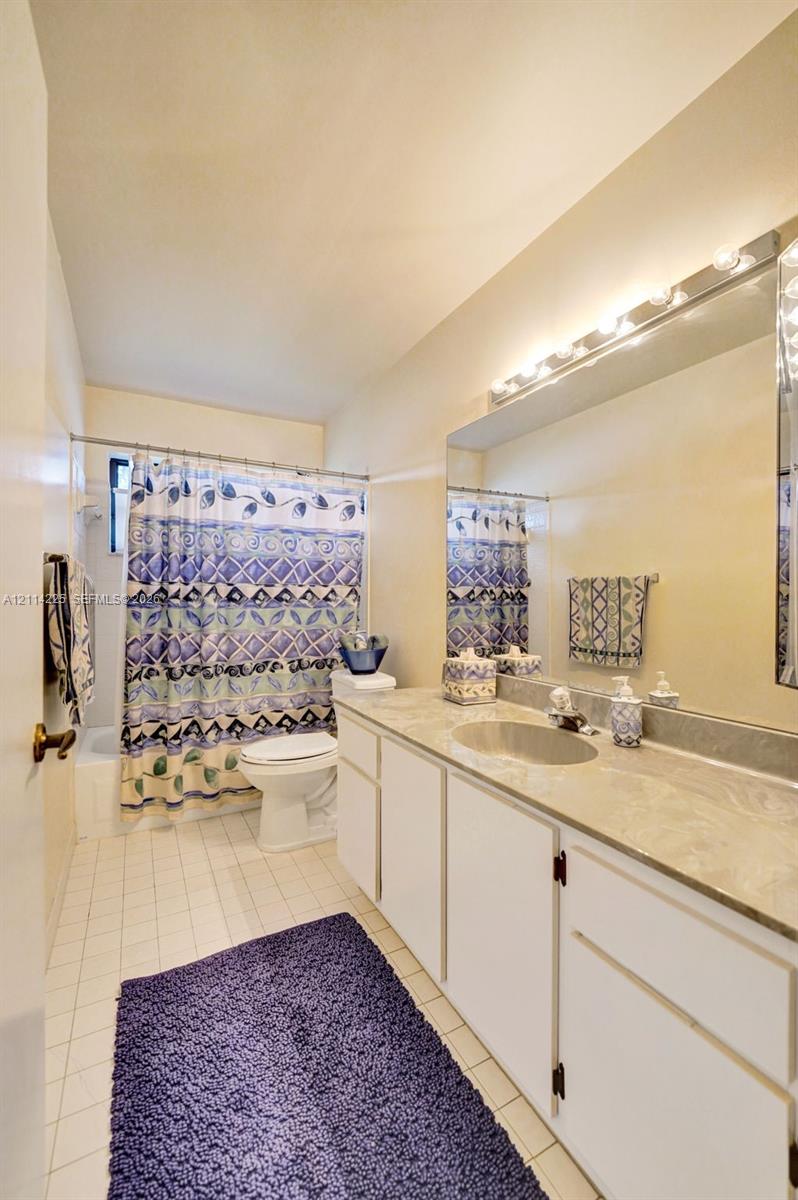 Full-width vanity featuring a stone-composite countertop with an integrated basin, white shaker-style cabinetry, large wall-mounted mirror, and multi-bulb fixture