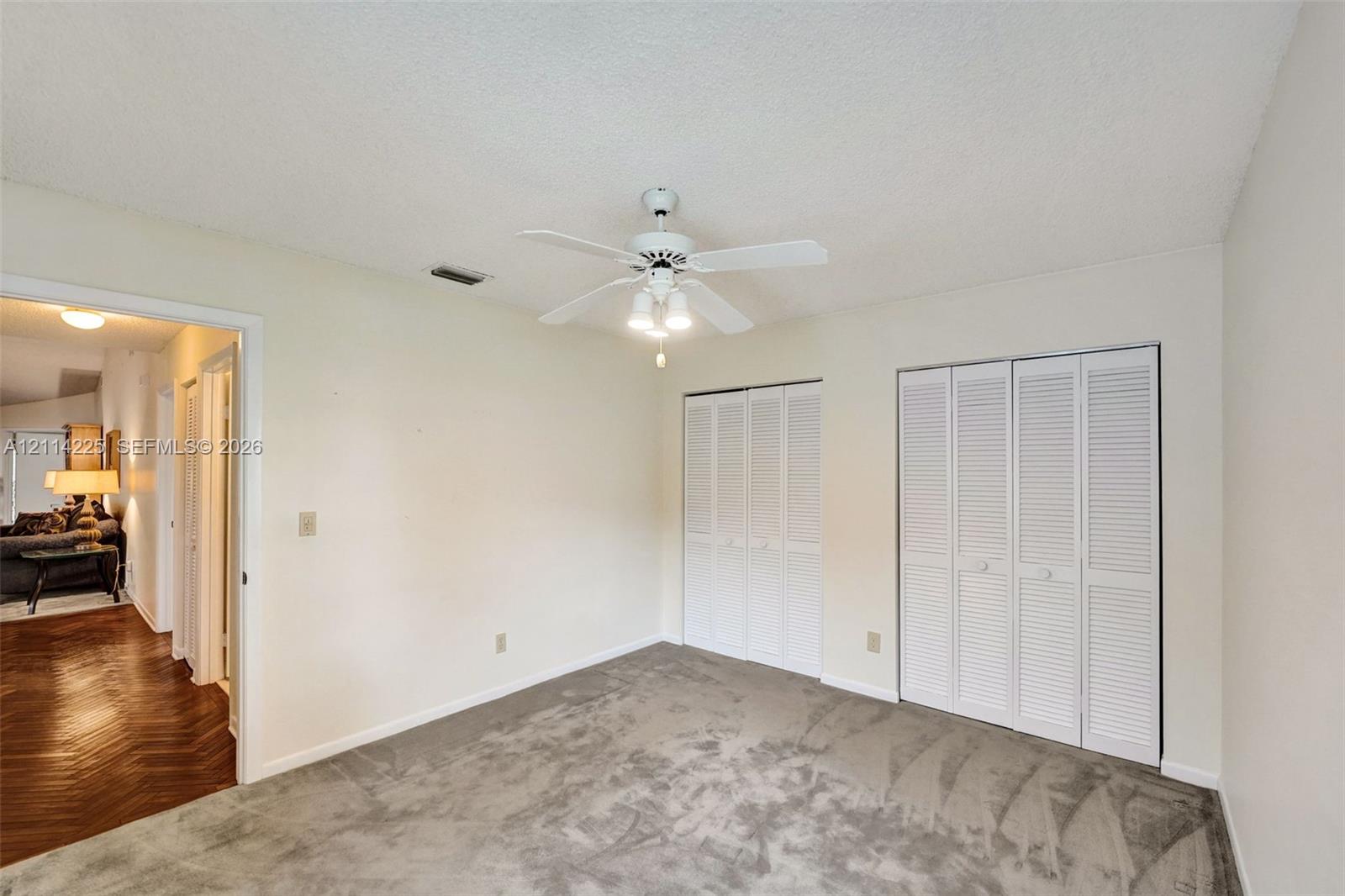 Neutral-toned carpet, dual white louvered-door closets, and a central ceiling fan with multi-bulb light fixture