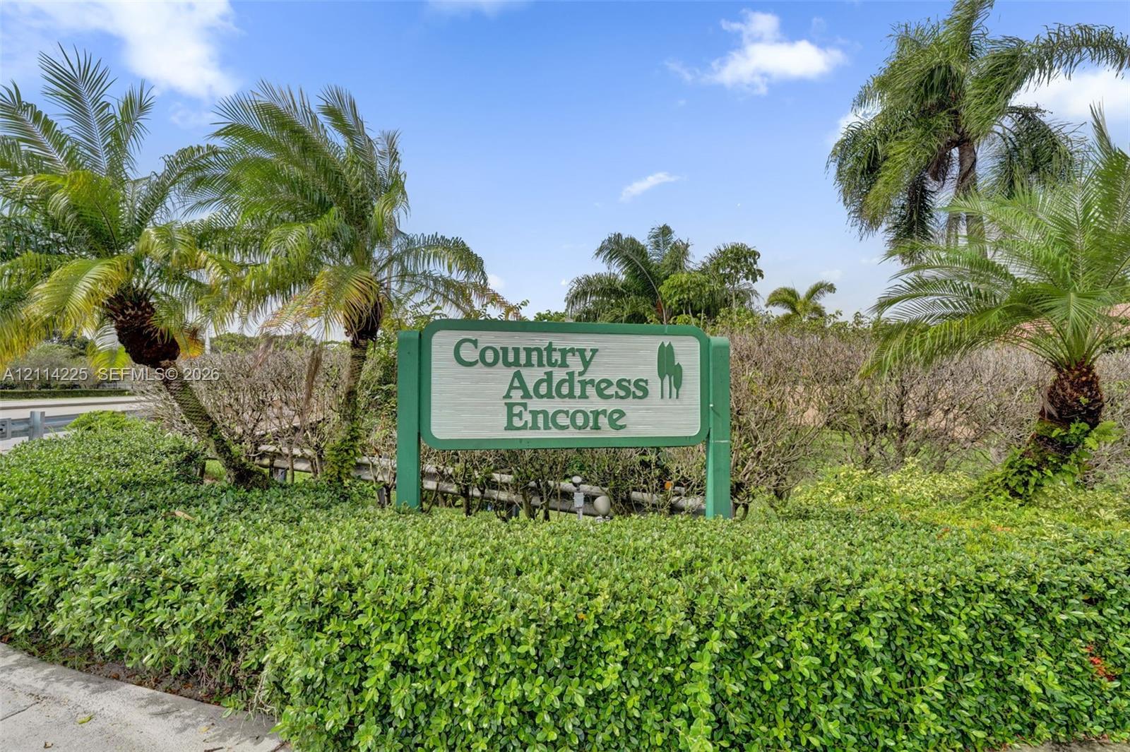 Community signage featuring professional landscaping, manicured hedges, and mature palm trees