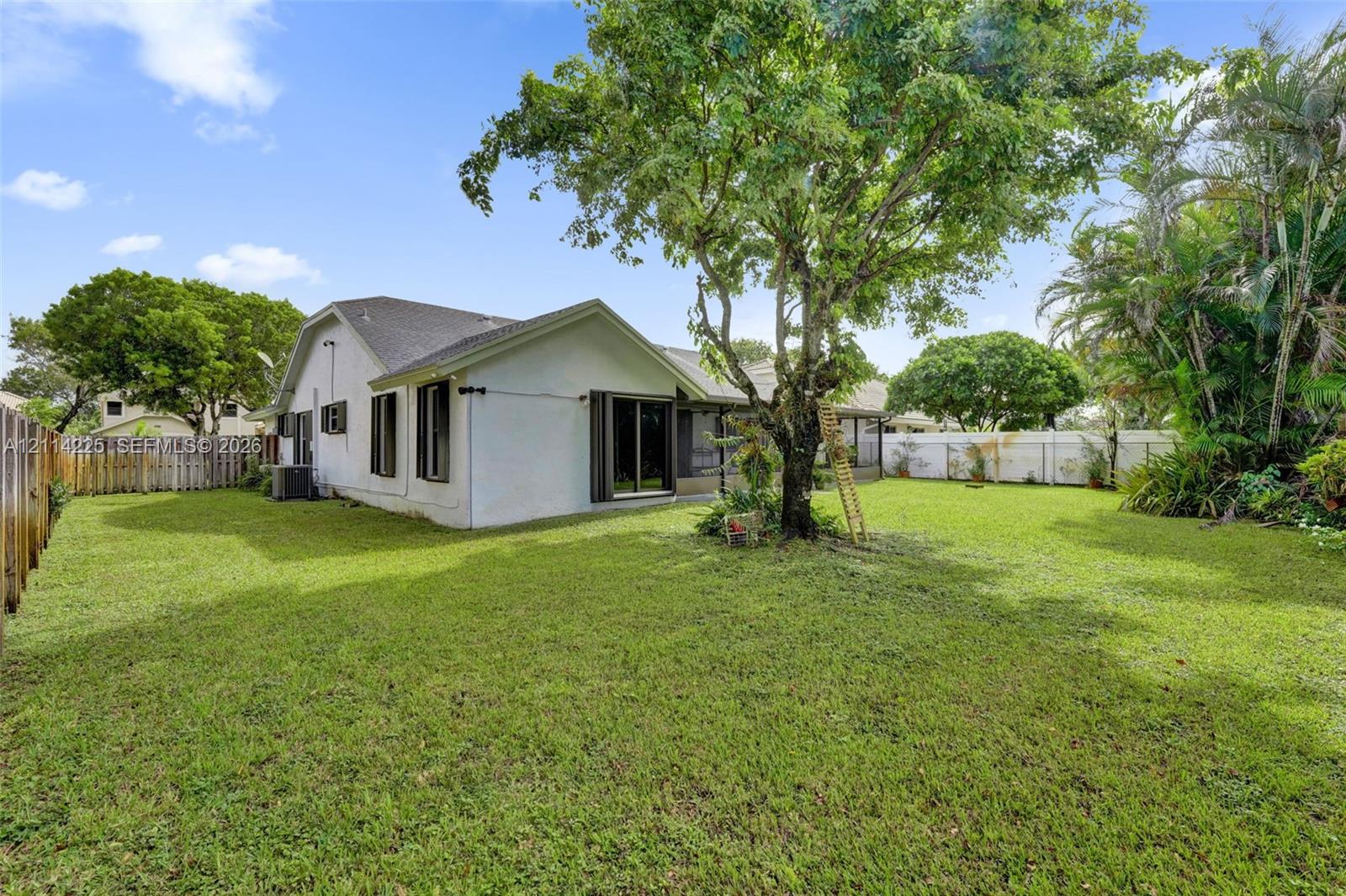 Expansive backyard featuring a mature canopy tree, perimeter wood fencing, white vinyl privacy screening, and low-maintenance landscaping