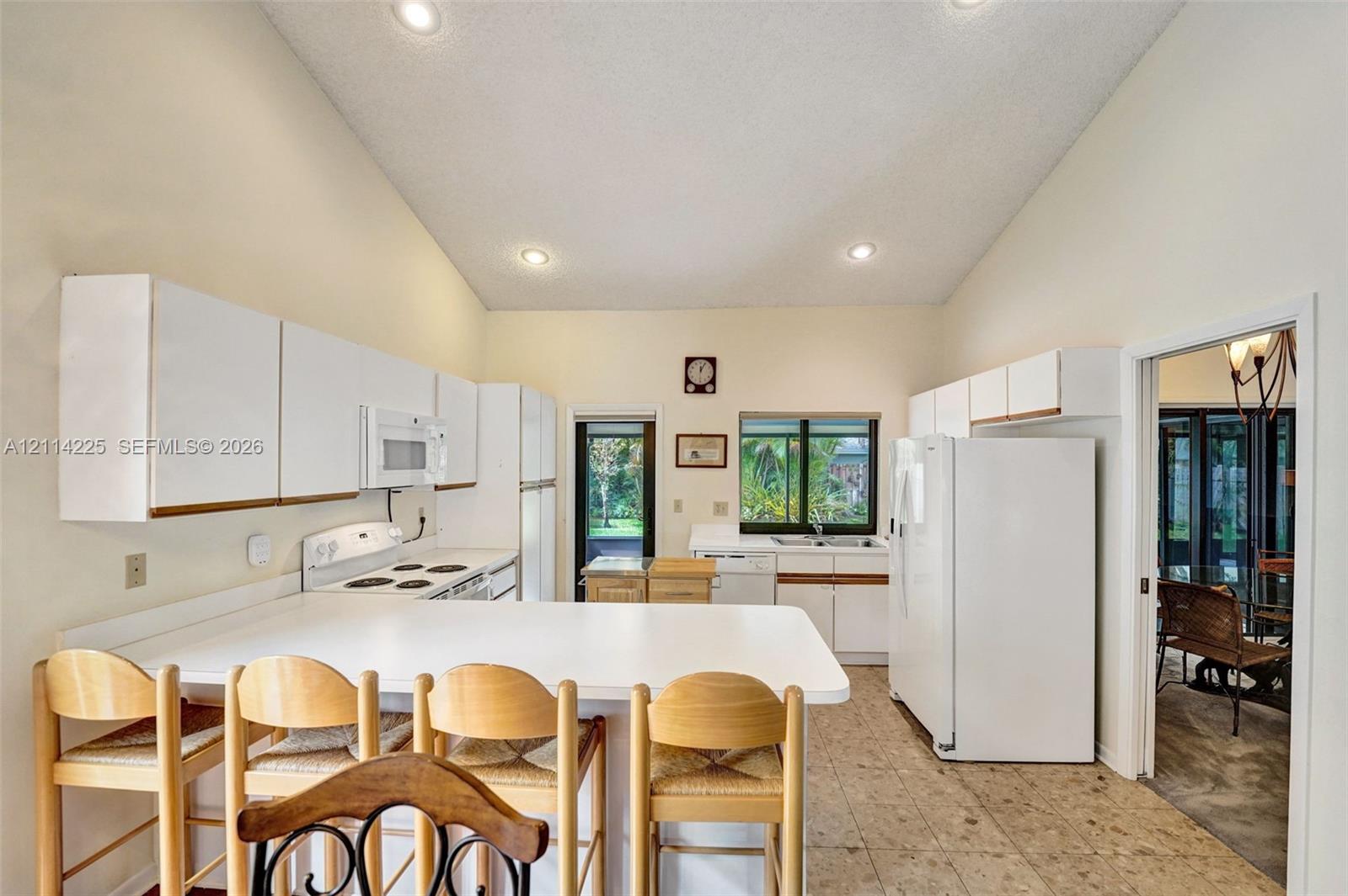 Kitchen featuring high vaulted ceilings, recessed lighting, white cabinetry, a breakfast bar, and tile flooring