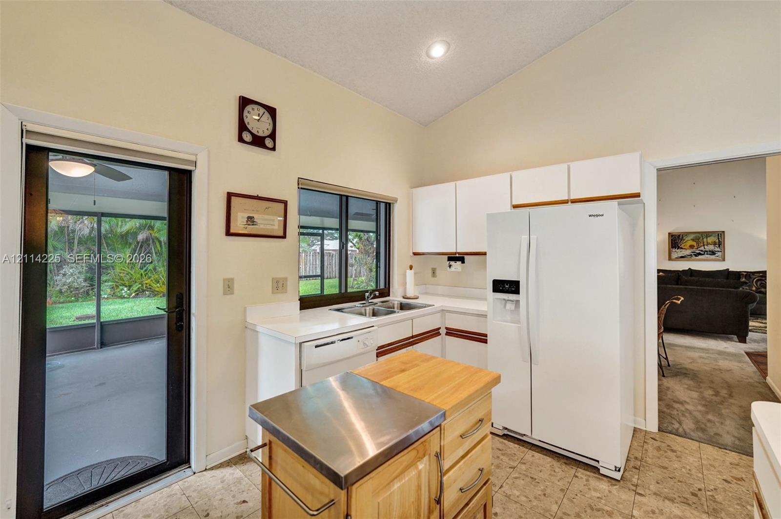 Kitchen featuring white cabinetry, solid-surface countertops, double-basin sink, and tile flooring, with an integrated glass door providing outdoor access