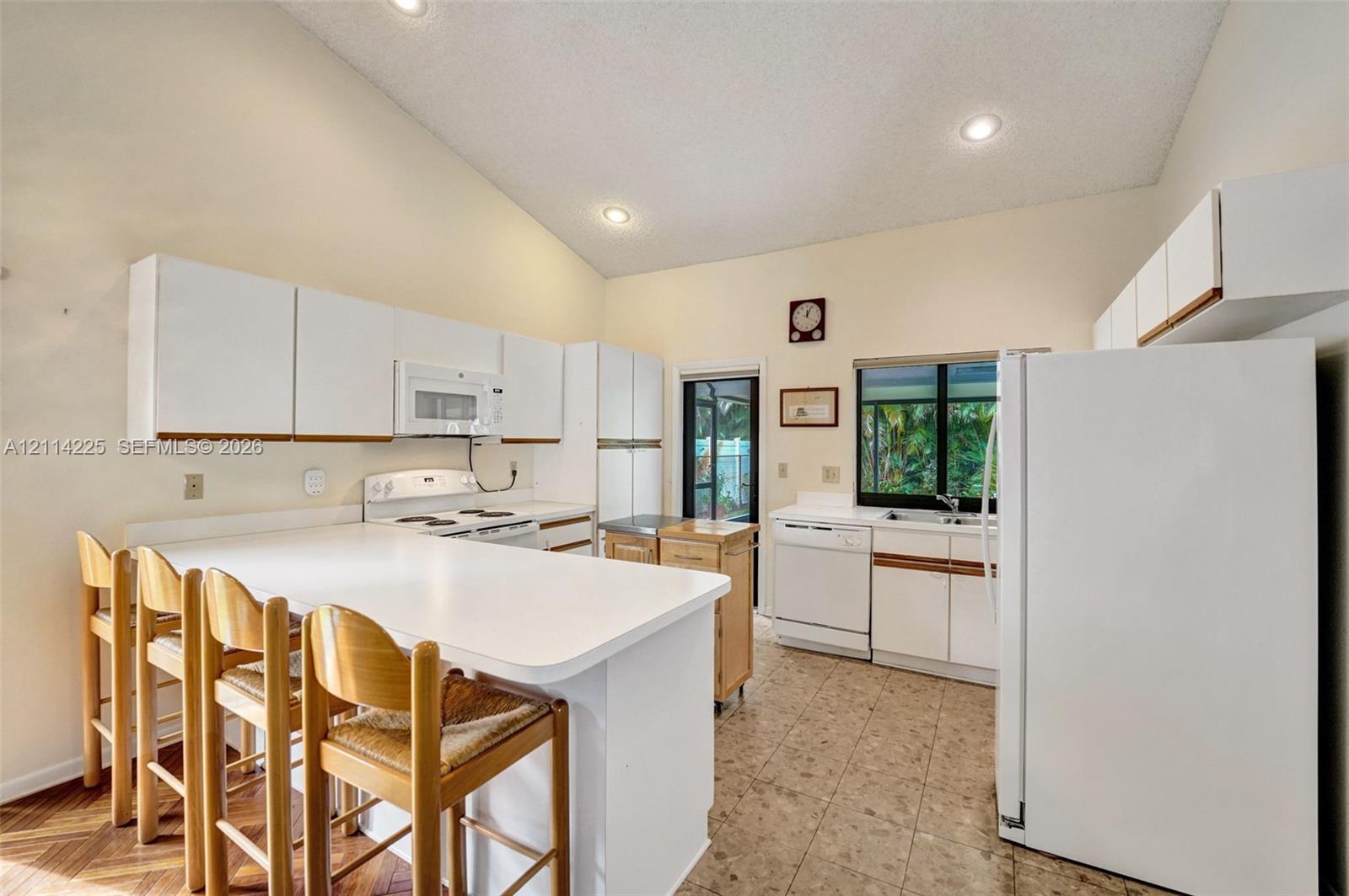 Kitchen featuring a vaulted ceiling, recessed lighting, white cabinetry, a breakfast bar, and tile flooring