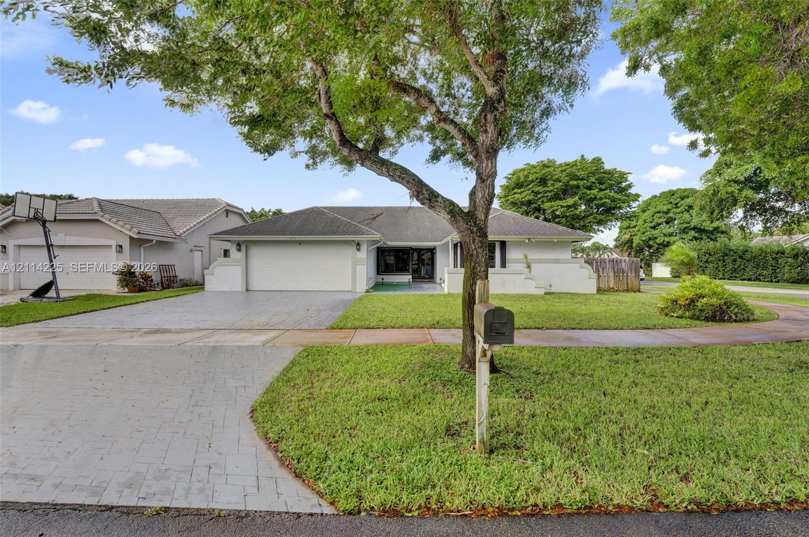 Single-story residence featuring a tile roof, paved driveway, two-car garage, and established landscaping