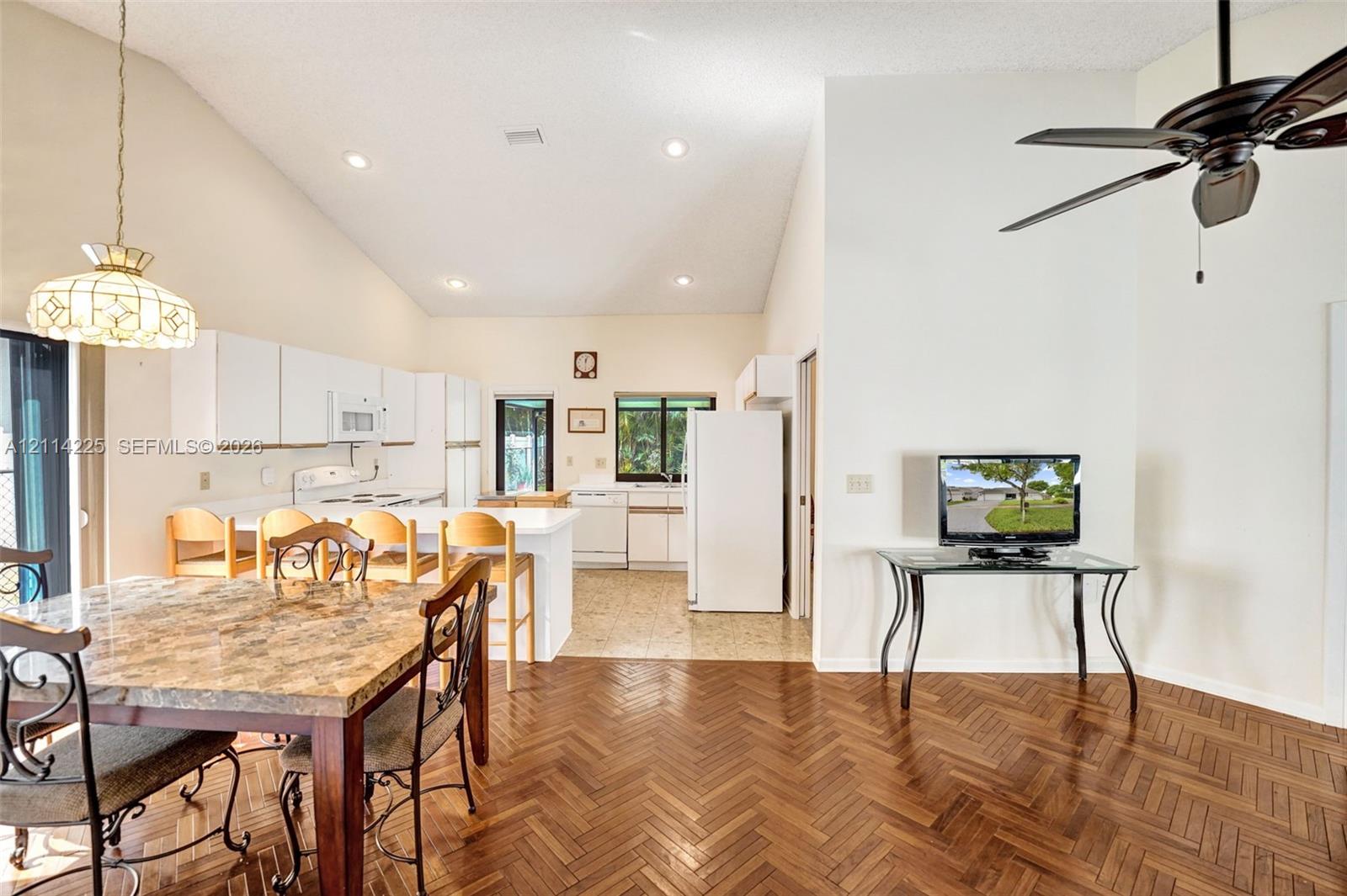 Open-concept interior featuring vaulted ceilings, herringbone-patterned wood flooring, recessed lighting, and a breakfast bar with built-in cabinetry