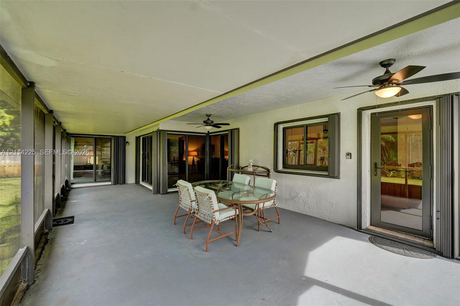 Screened-in patio featuring a concrete floor, multiple sliding glass door entries, and dual overhead ceiling fans
