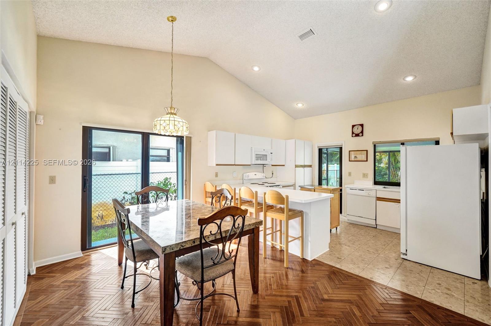 Open-concept kitchen and dining area featuring vaulted ceilings, herringbone-pattern wood-finish flooring, a breakfast bar, and sliding glass doors