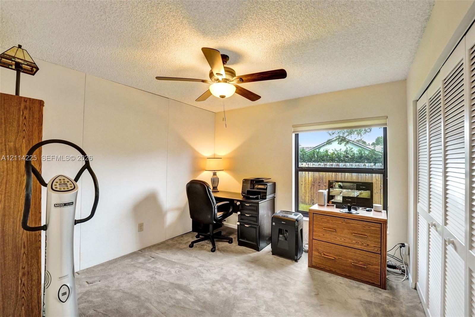 Room featuring neutral carpeted flooring, a ceiling fan with integrated light fixture, and floor-to-ceiling closet with louvered doors