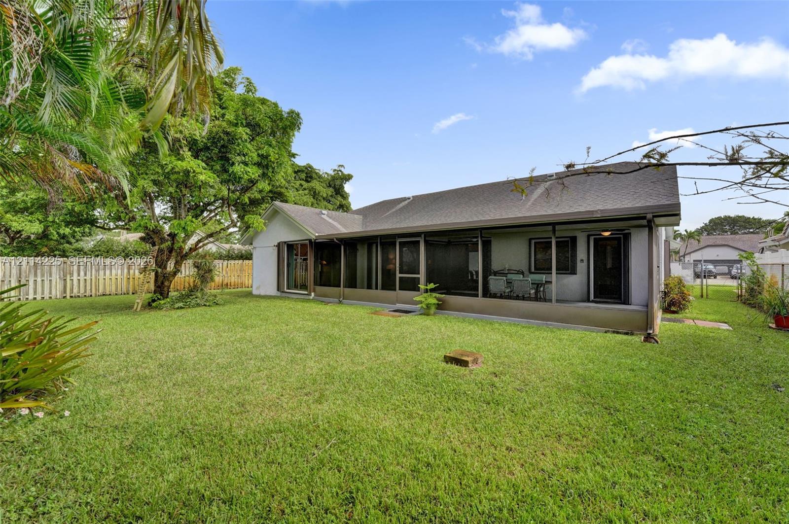 Spacious backyard featuring a manicured lawn, mature trees, and perimeter wood-style fencing, complete with a screened-in rear porch