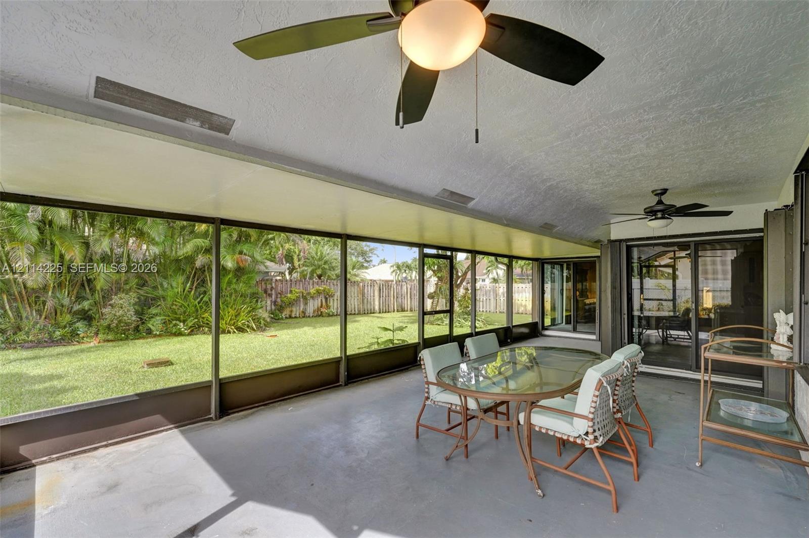 Screened-in lanai featuring a solid ceiling with dual overhead fans, concrete flooring, and sliding glass door access to the backyard
