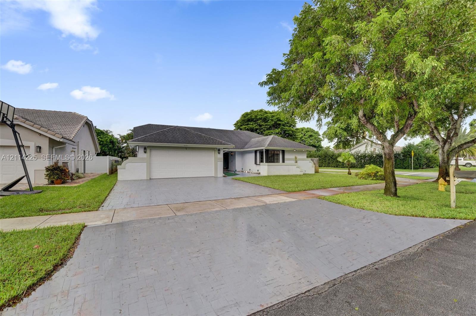 Single-story exterior featuring a textured concrete driveway, attached two-car garage, bay window, and mature landscaping
