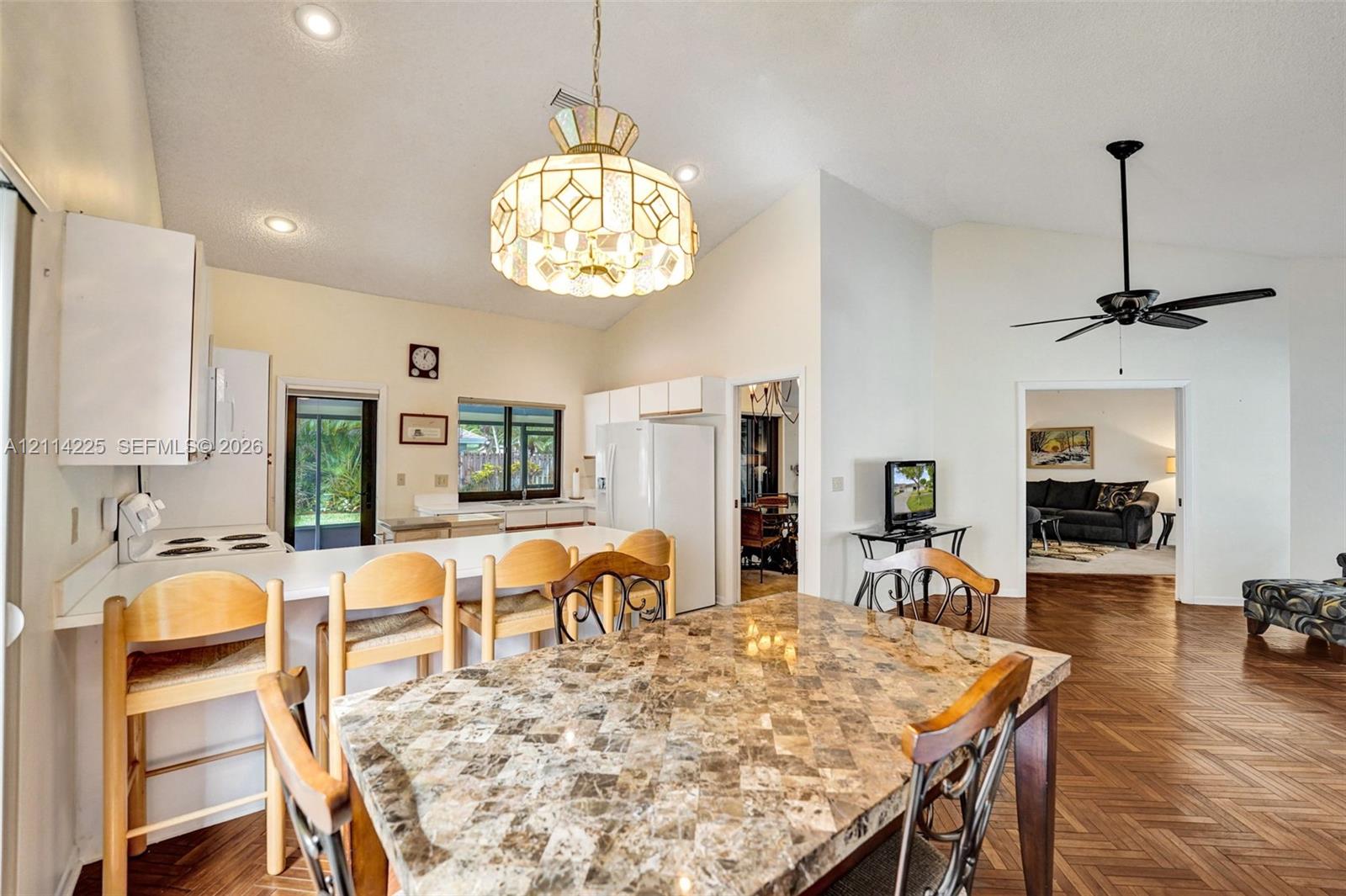 Open-concept kitchen area featuring vaulted ceilings, recessed lighting, a decorative pendant light fixture, wood-finish flooring, and a stone-topped breakfast bar